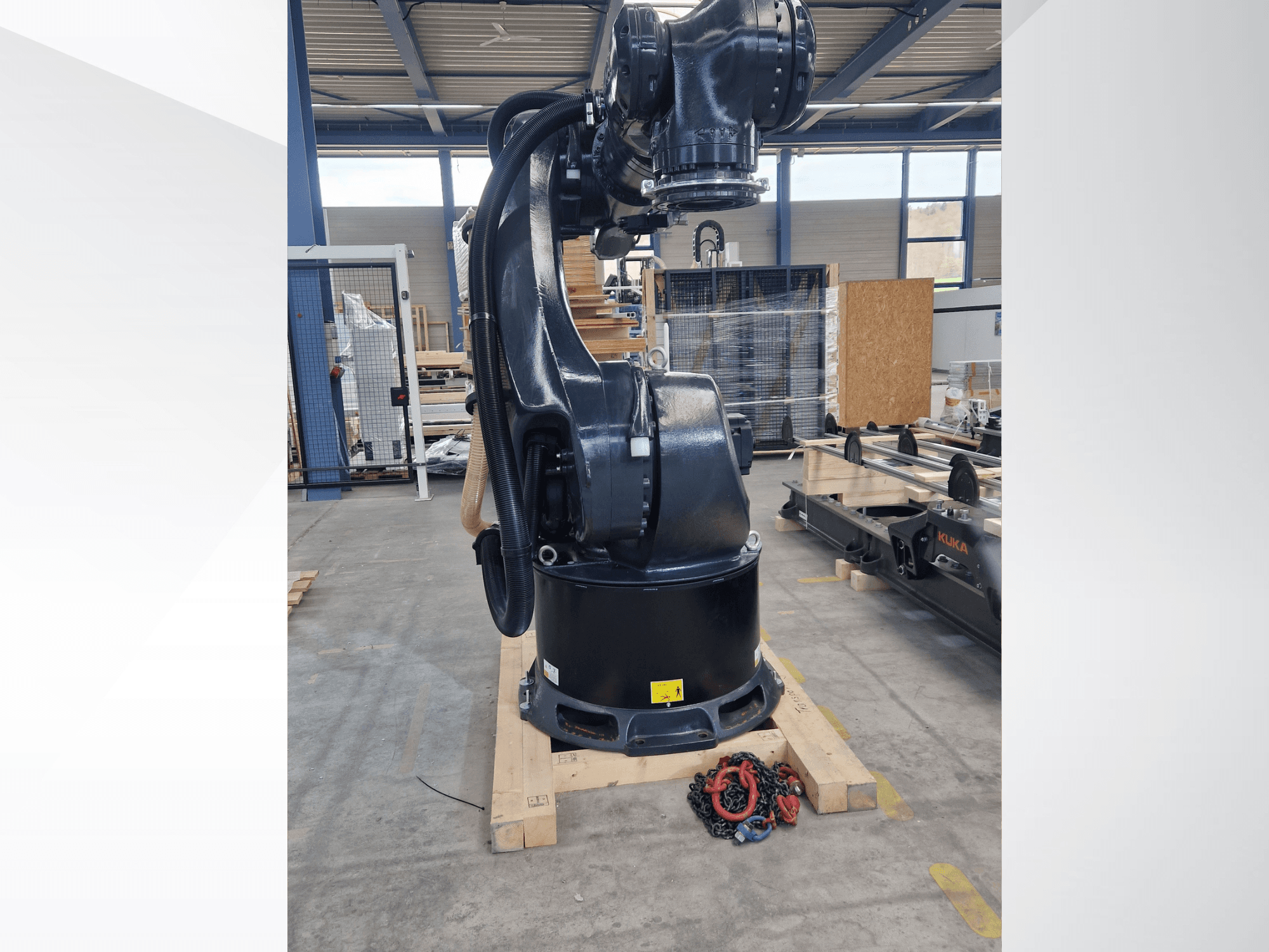 Ramię robota KUKA KR 340 R3330 w magazynie, widok z boku ukazujący jego podstawę i kable, z łańcuchami na pierwszym planie.
