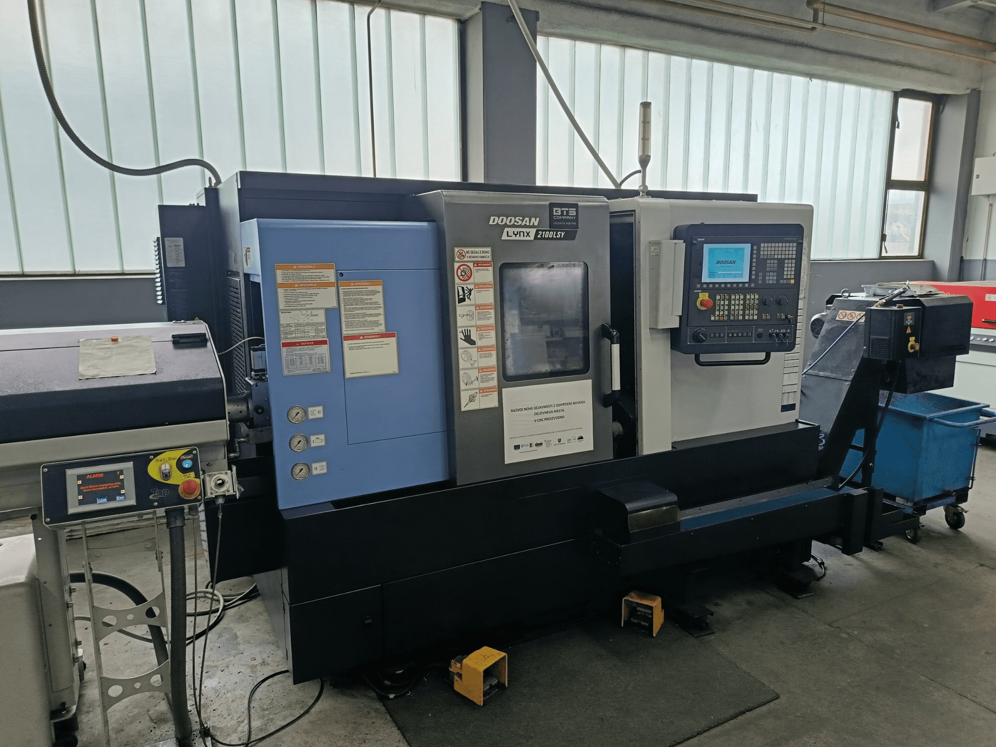 Centrum frezarskie DOOSAN LYNX 2100 LSY, widok z boku przedstawiający panel sterowania i przyciski operacyjne z widocznymi etykietami informacyjnymi.