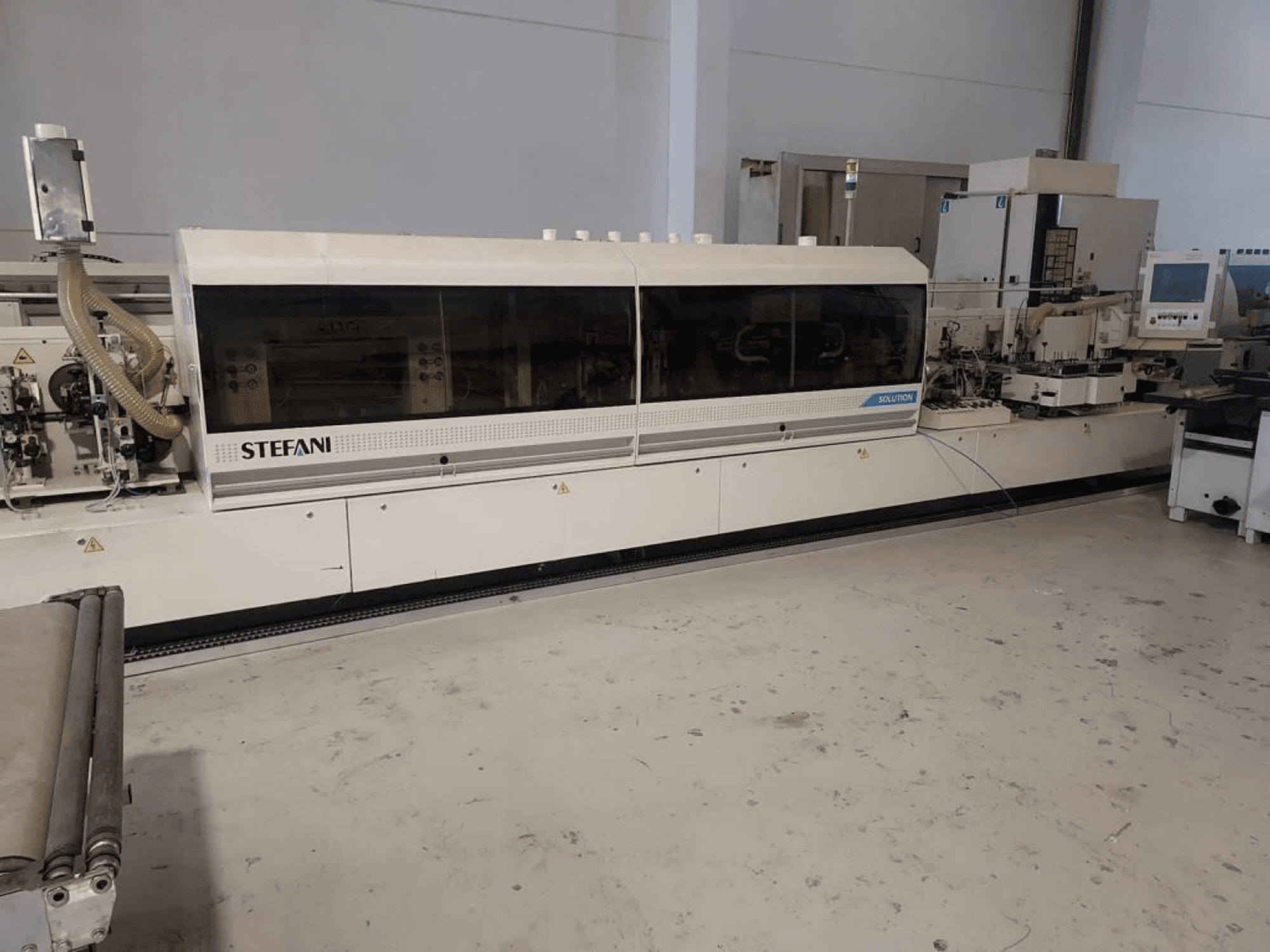 Okleiniarka Stefani Solutions, widok z przodu, z widocznym systemem odsysania pyłu i panelem sterowania, w warunkach warsztatowych.