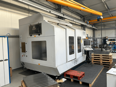 Maszyna CNC Spinner VC 1650, widok z przodu, z panelem sterowania, dużymi oknami i paletami ułożonymi w pobliżu w otoczeniu warsztatu.