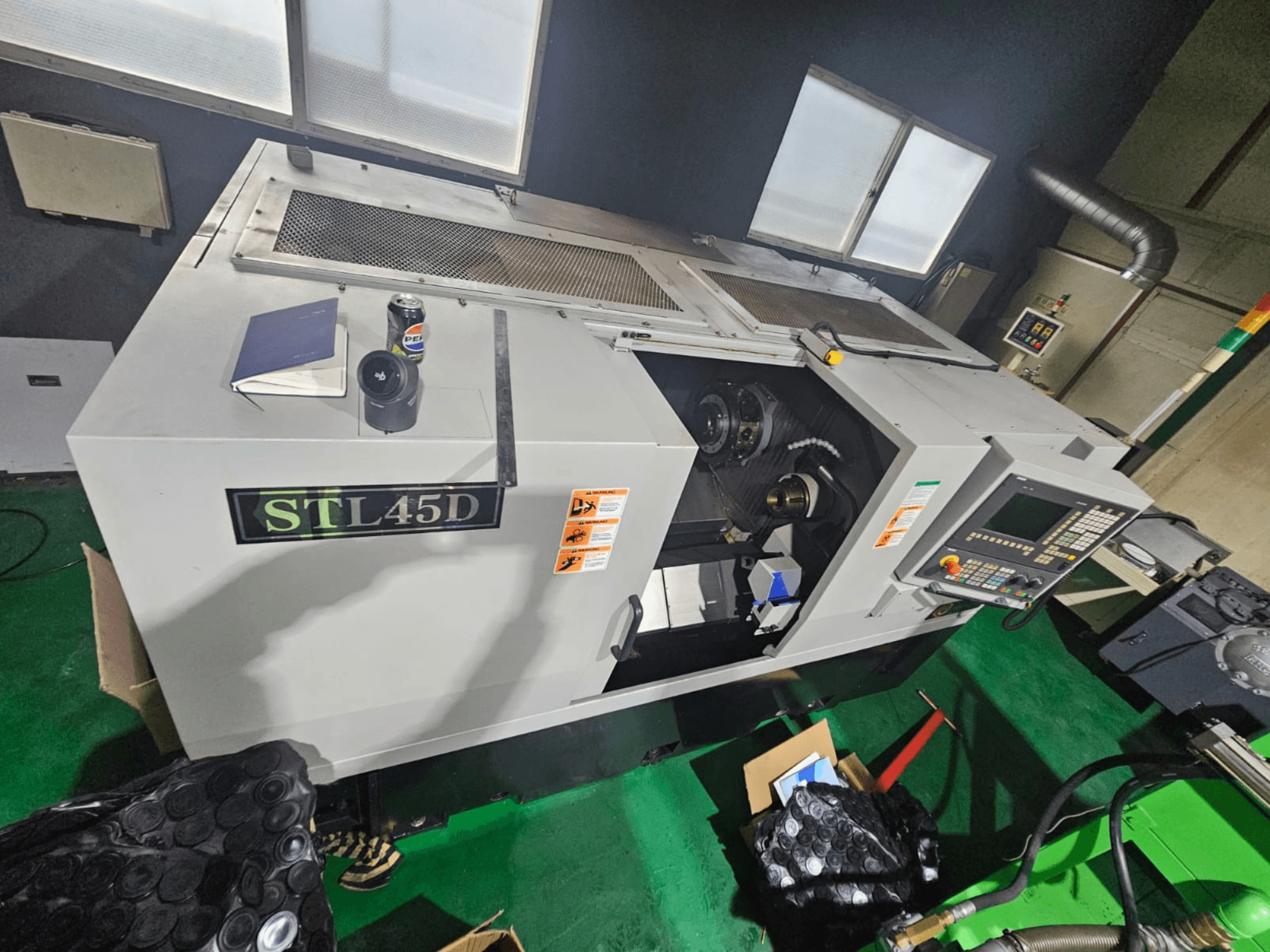 Maszyna CNC STL45D widziana z góry, z panelem sterowania, częścią cylindryczną, notebookiem i puszką na górze.