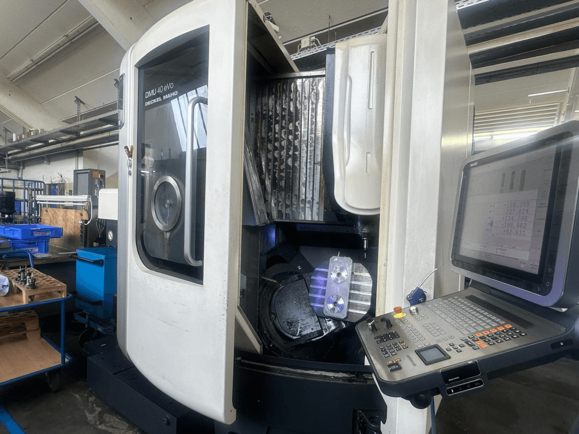 Frezarka DMU 40 eVo firmy Deckel Maho w warsztacie, widok z przodu, pokazujący panel sterowania i metalowy element we wrzecionie.