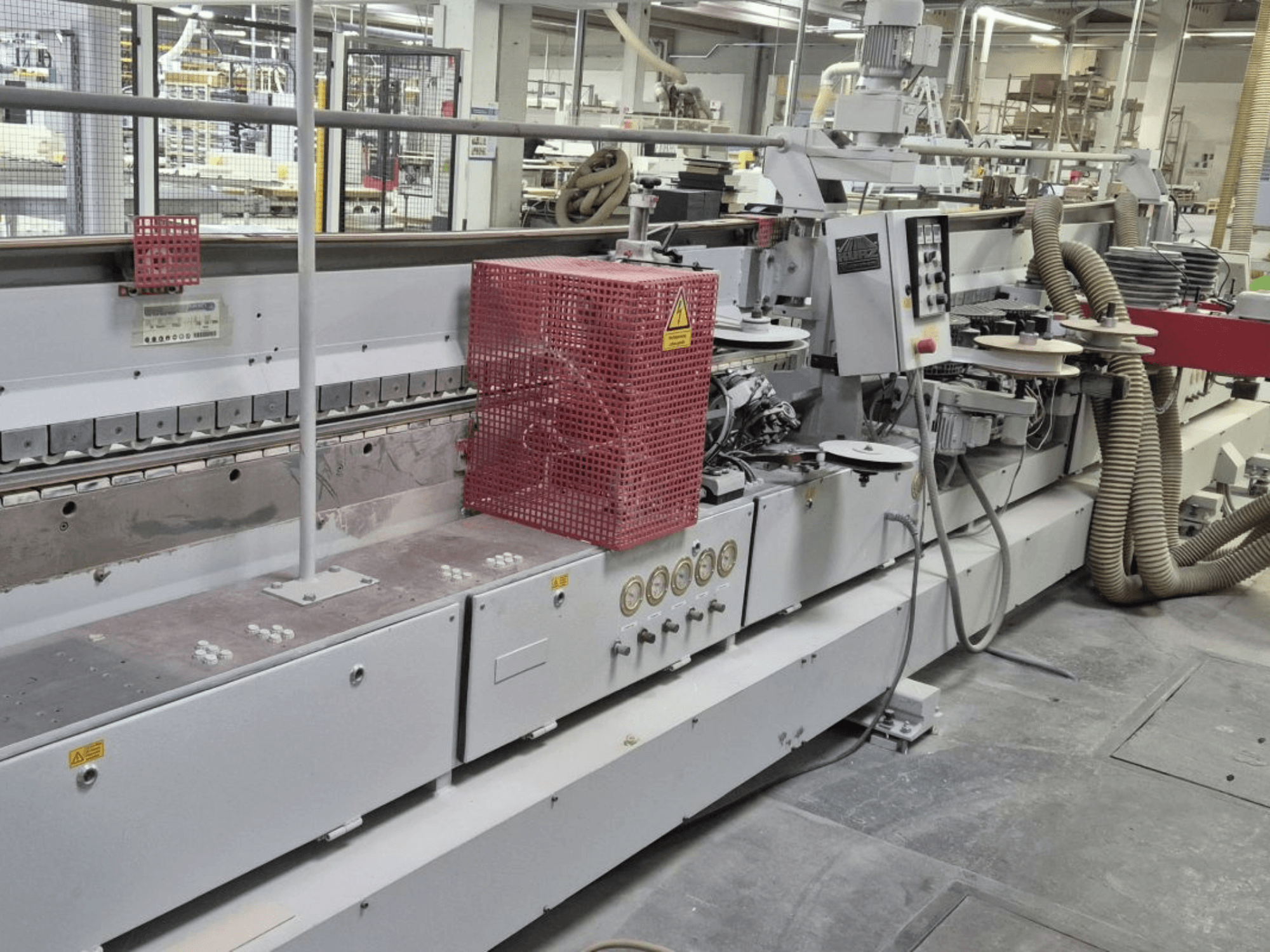 Maszyna do oklejania krawędzi z panelem sterowania, wężami ssącymi i czerwoną osłoną bezpieczeństwa, widziana z boku.