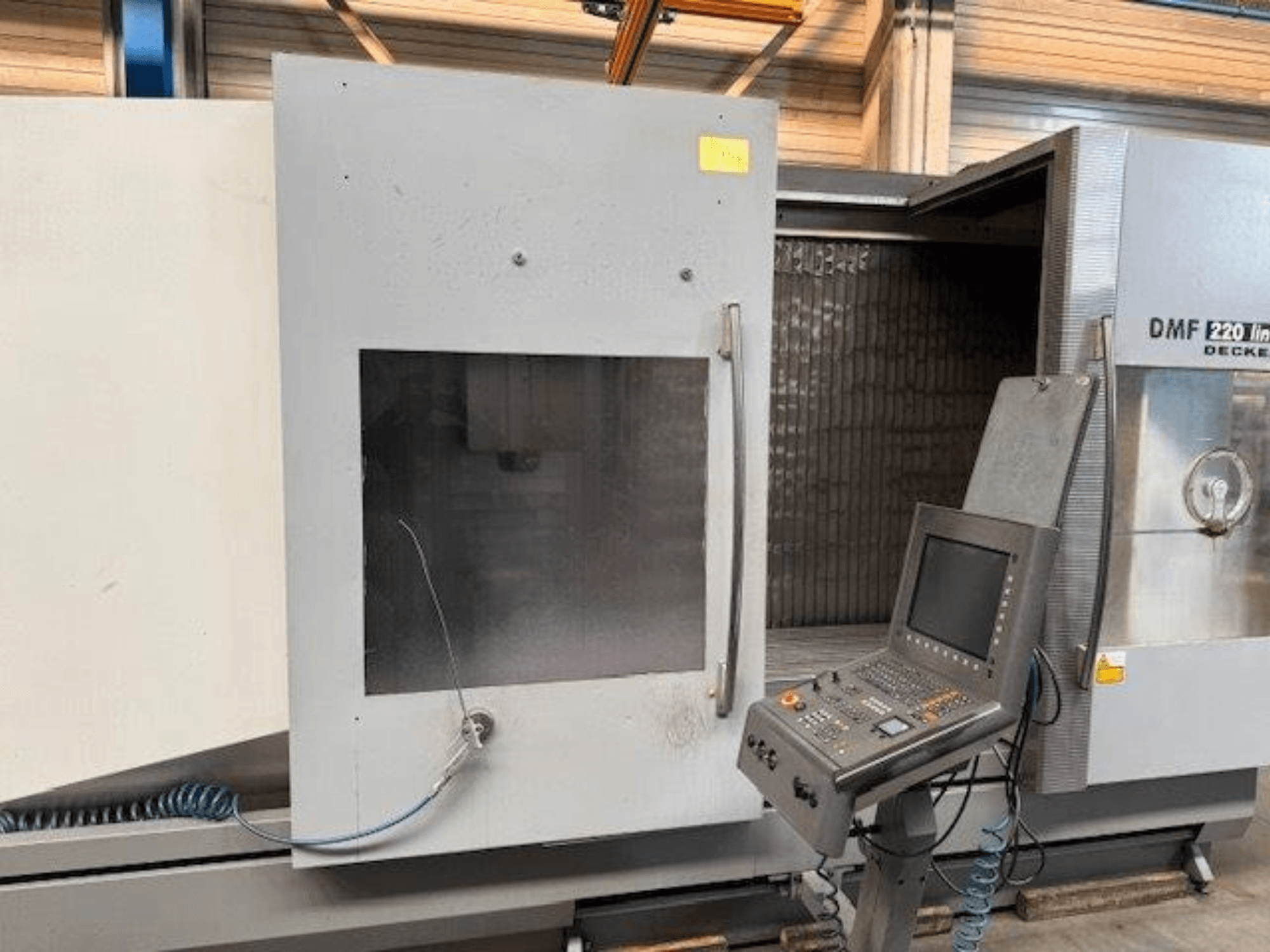 Widok z przodu pionowego centrum obróbczego DECKEL MAHO DMF 220 Linear, przedstawiający panel sterowania i otwarte drzwi maszyny.