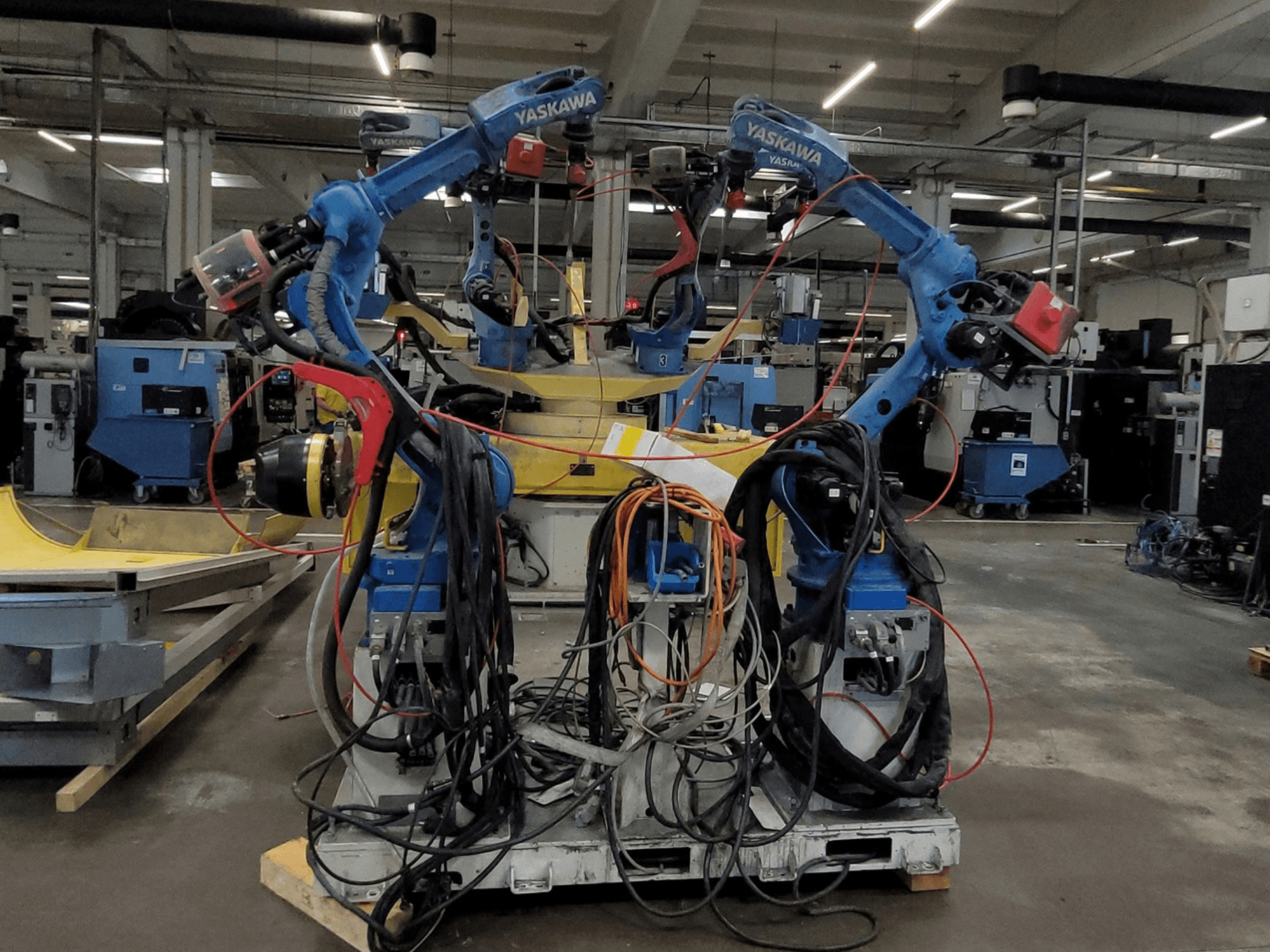 Komórka spawalnicza Yaskawa RWC L1_OS 15330 – widok z przodu, przedstawiająca dwa niebieskie roboty z rozległą siecią kabli i narzędziami spawalniczymi.