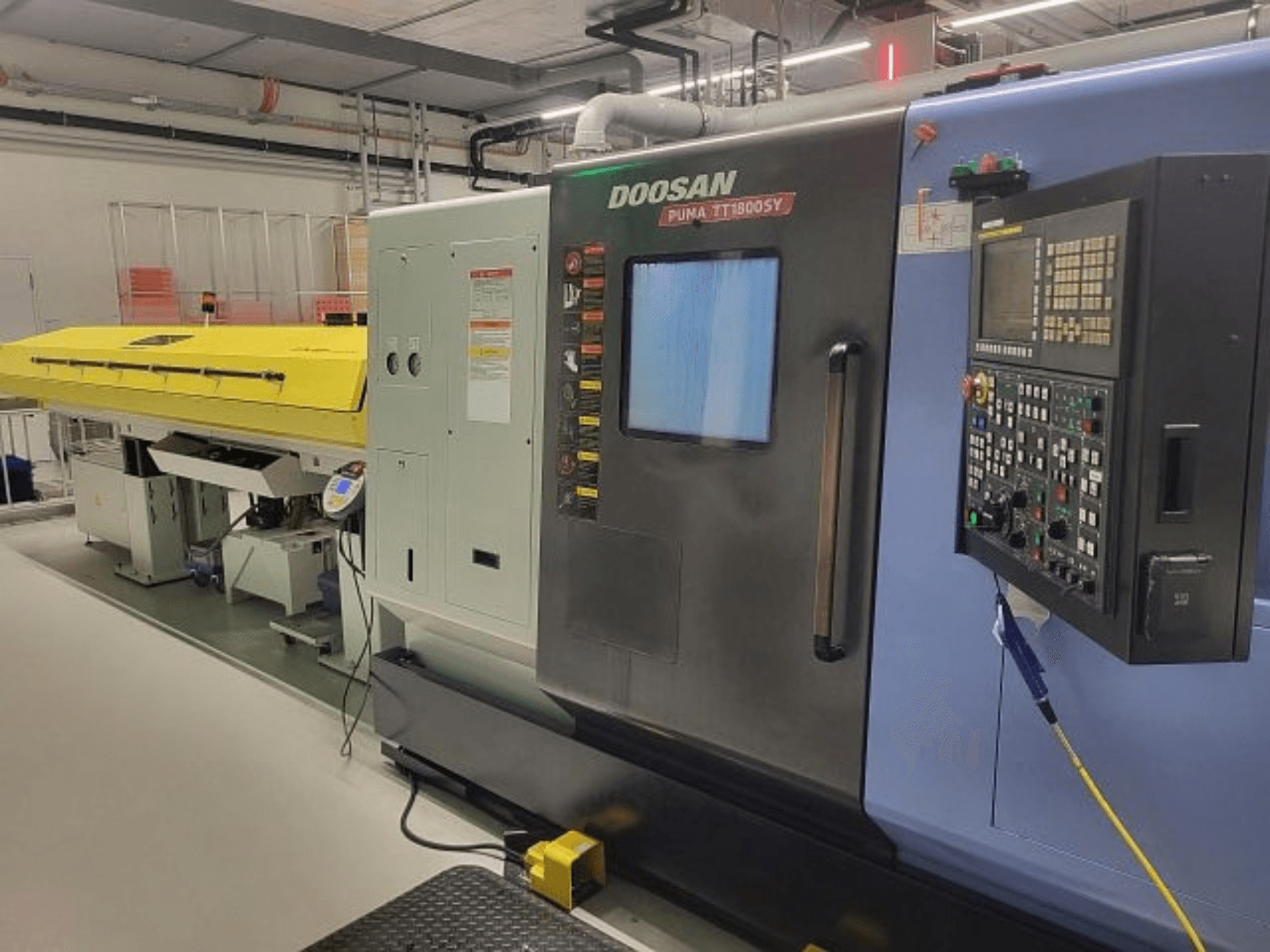 Centrum tokarsko-frezarskie DOOSAN PUMA TT 1800 SY, widok z przodu z panelem sterowania i żółtą osłoną, otoczenie przemysłowe.