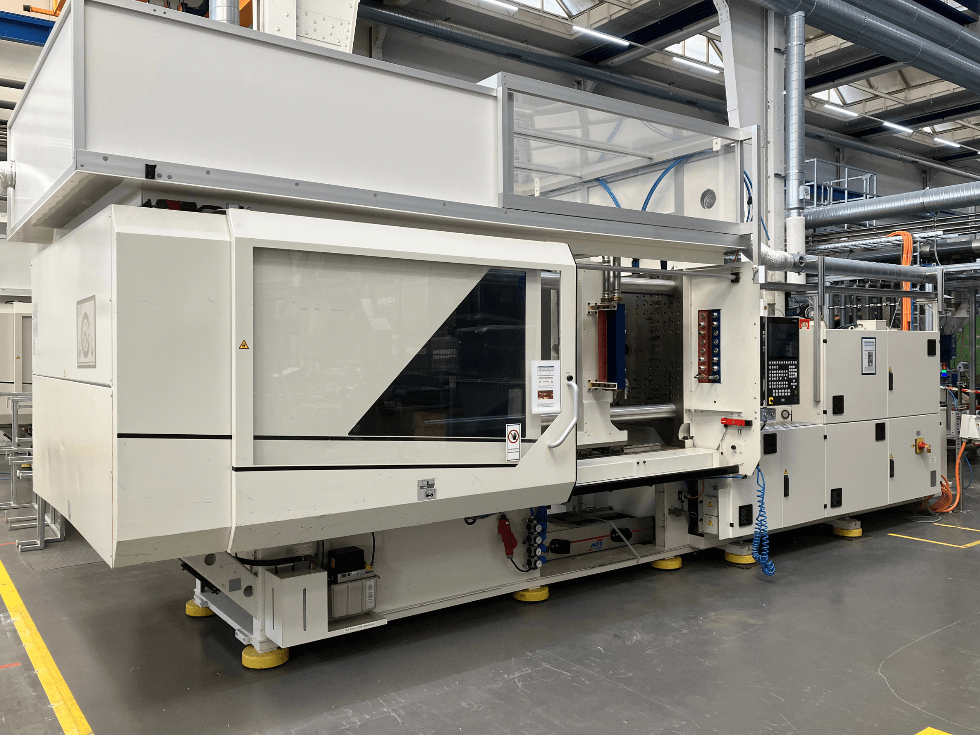 Widok z boku wtryskarki, model AET, z panelem sterowania i przezroczystymi pokrywami, w warunkach przemysłowych.