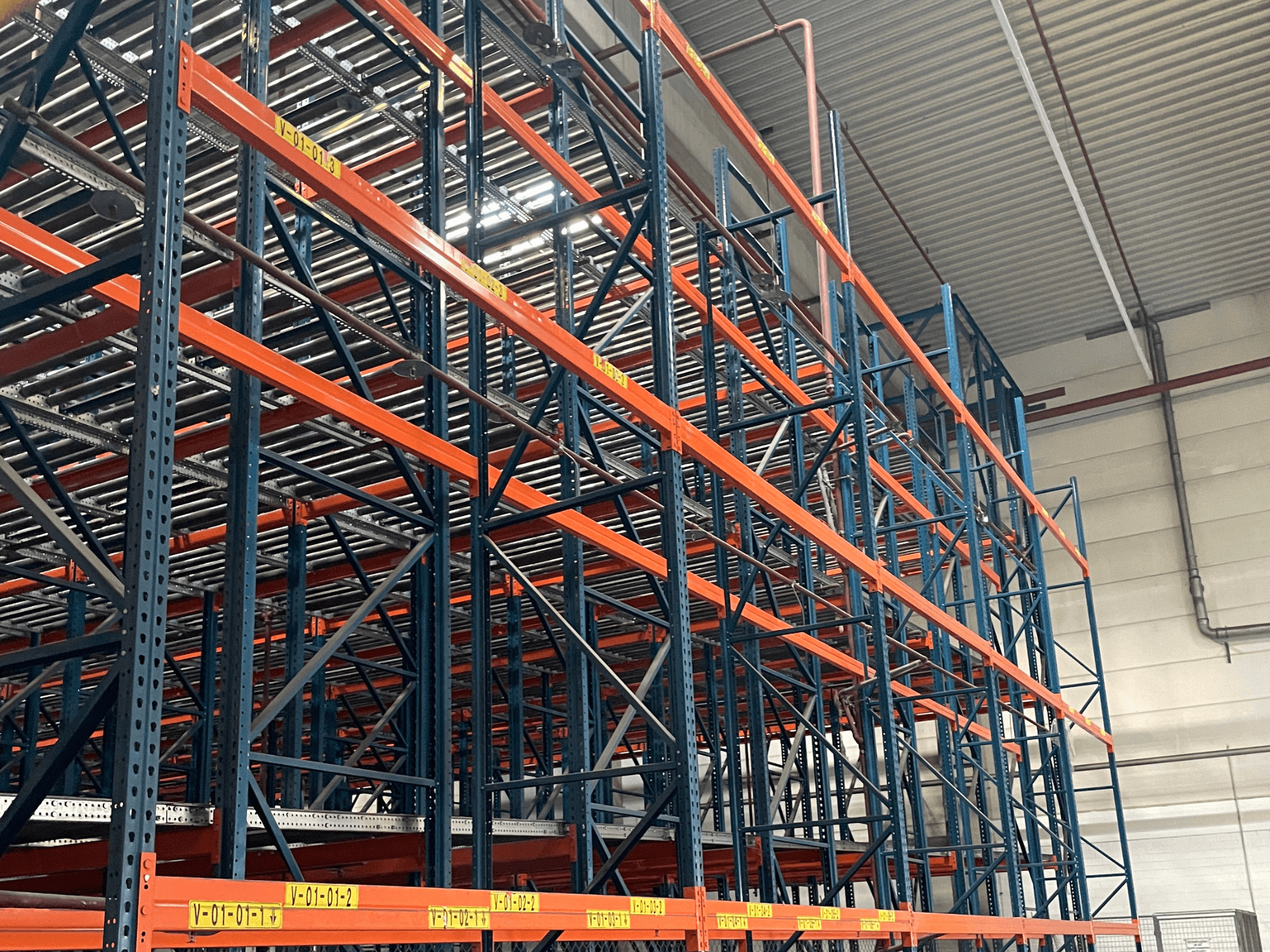 FL SYSTEME F05.10 System obsługi palet FLG w magazynie, pokazany z boku, wyposażony w wytrzymałe pomarańczowe i niebieskie regały.