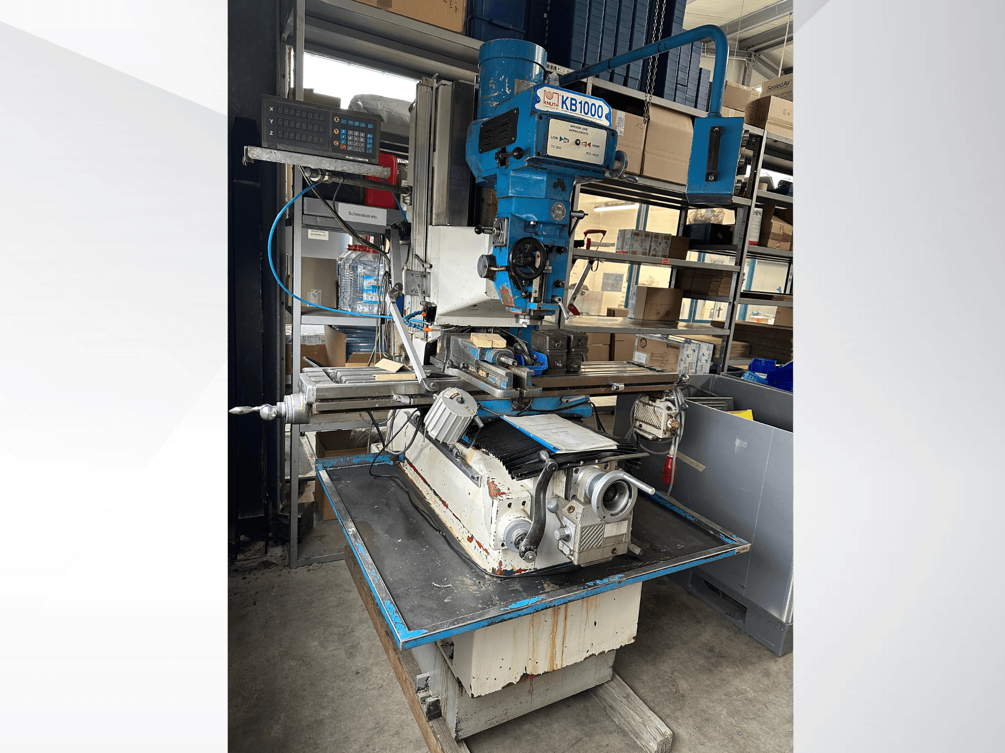 Frezarka pionowa KB1000 z wyświetlaczem cyfrowym, widok z boku przedstawiający stół, wrzeciono i uchwyt narzędziowy.