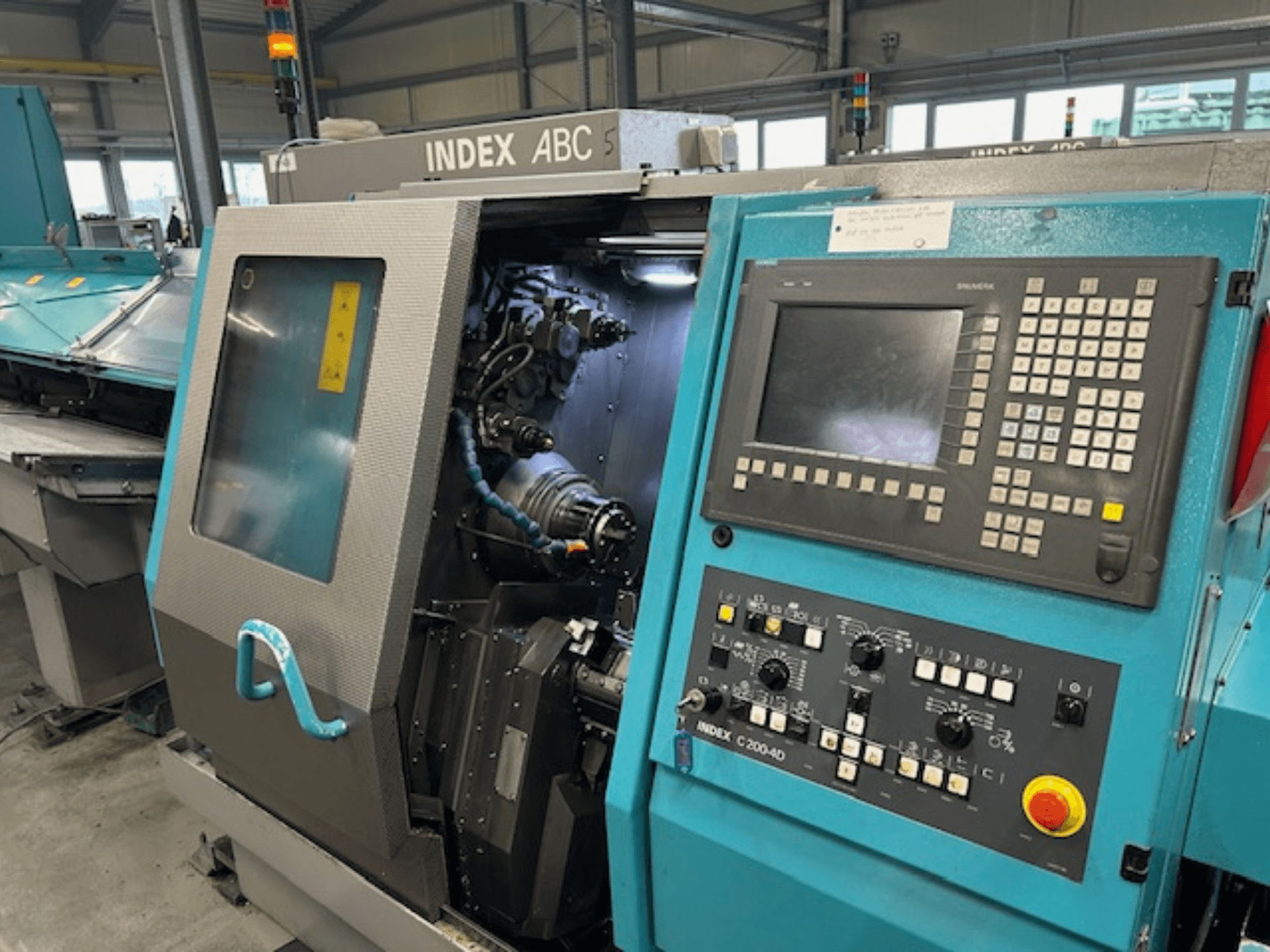 Widok z przodu tokarki CNC INDEX C200-AD z panelem sterowania, widocznymi elementami wewnętrznymi i zabezpieczeniami.