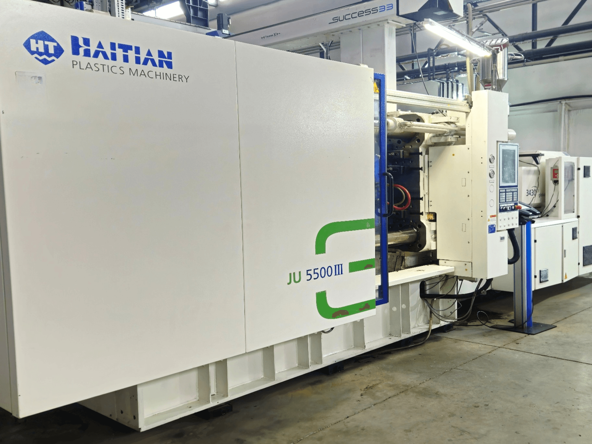 Haitańska maszyna do tworzyw sztucznych JU 5500III w fabryce, widok z przodu przedstawiający panel sterowania i obszar produkcyjny.