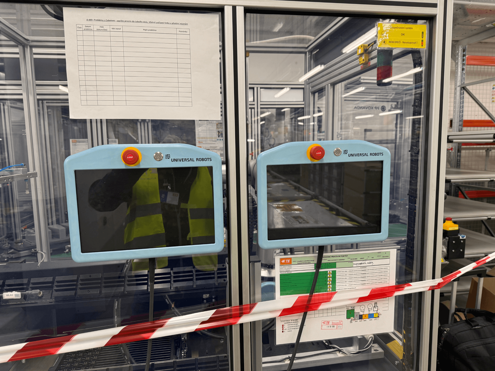 Panel sterowania dla ramienia robota Universal Robots UR5 e, wyposażony w dwa monitory, przyciski zatrzymania awaryjnego i instrukcje bezpieczeństwa.