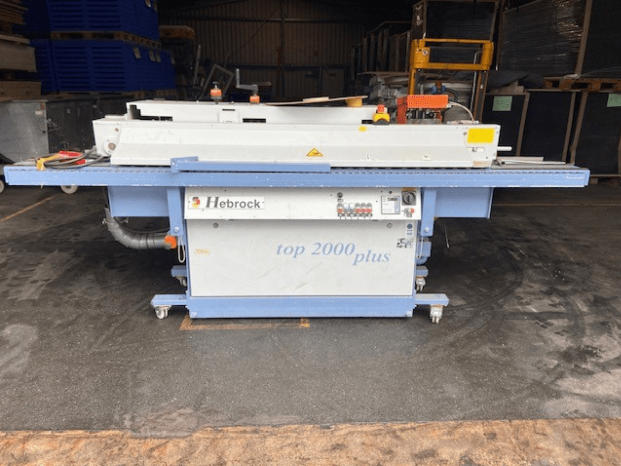 Hebrock Top 2000 Plus, widok z przodu; przemysłowa maszyna elektryczna z panelem sterowania, kółkami zapewniającymi mobilność i widocznymi etykietami bezpieczeństwa.