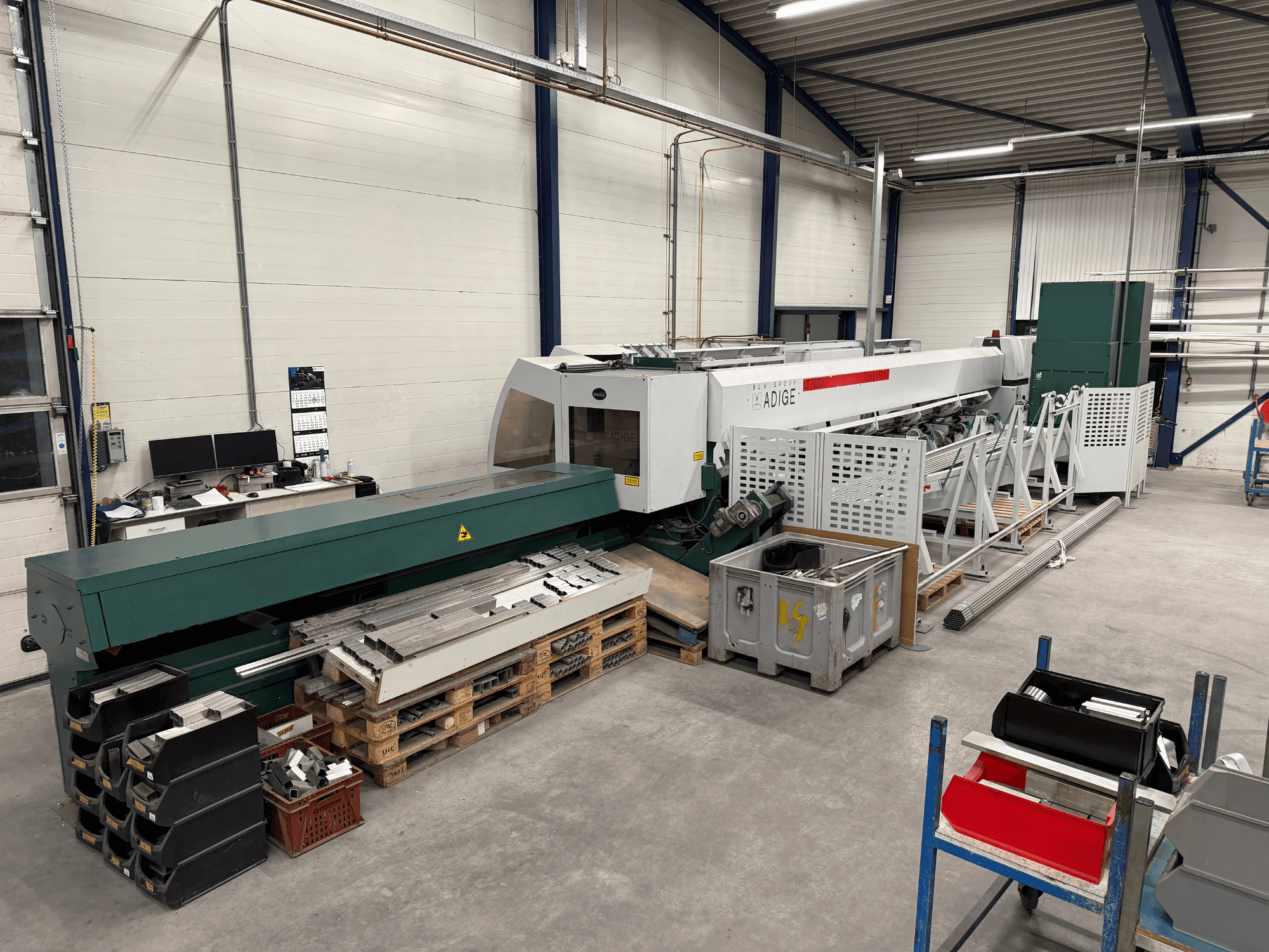 Maszyna do cięcia laserowego CO₂ BLM Adige LT702 w warsztacie, widok z boku, na którym widać metalowe elementy i bałagan w miejscu pracy.