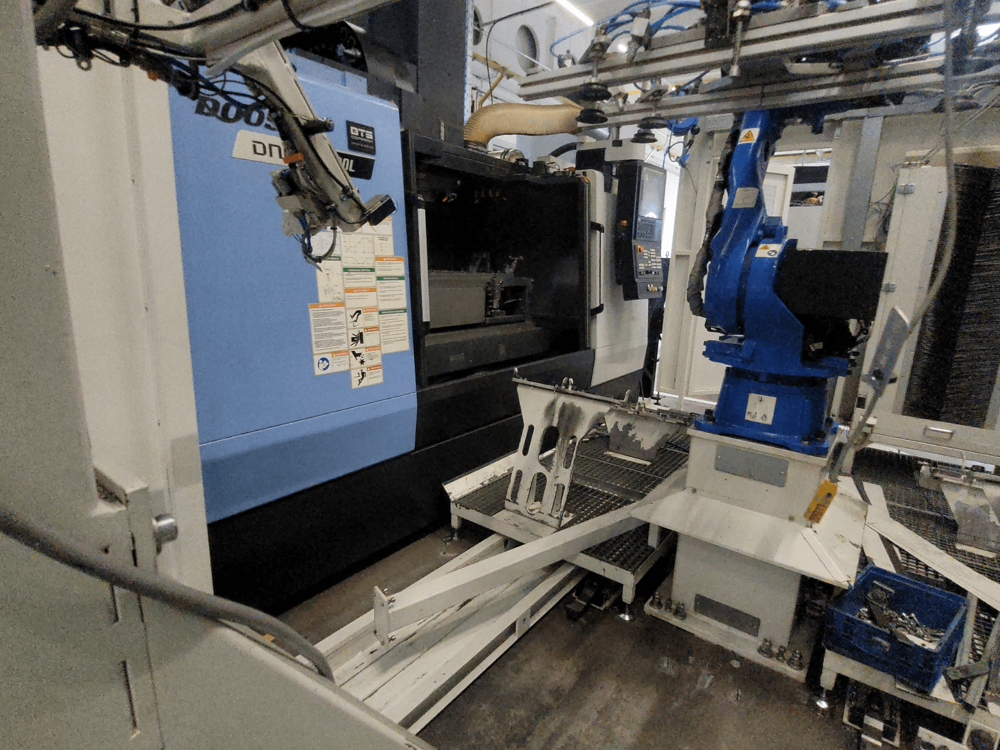 Widok z boku pionowego centrum obróbczego DOOSAN DNM 6700L, na którym widoczne są ramię robota i panel sterowania, przedstawiający konfigurację maszyny.