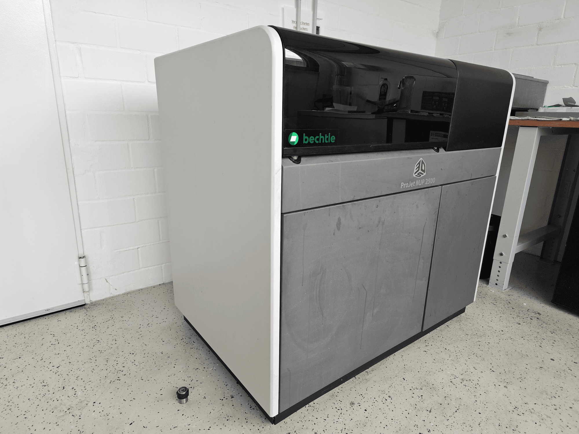 Drukarka 3D Systems ProJet MJP 2500 Plus do drukowania z tworzyw sztucznych – widok z przodu; charakteryzuje się elegancką konstrukcją z ciemną górną częścią i jasnym korpusem.