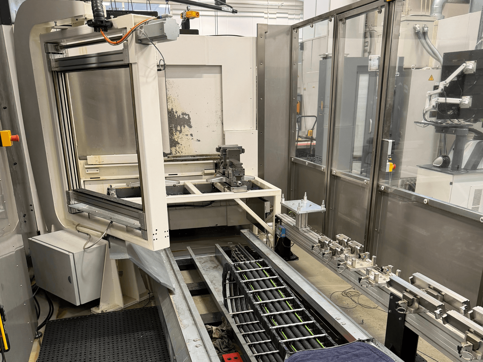 Zautomatyzowana przemysłowa stacja robocza z ramieniem robotycznym, systemem szyn i panelem sterowania w widoku z boku.