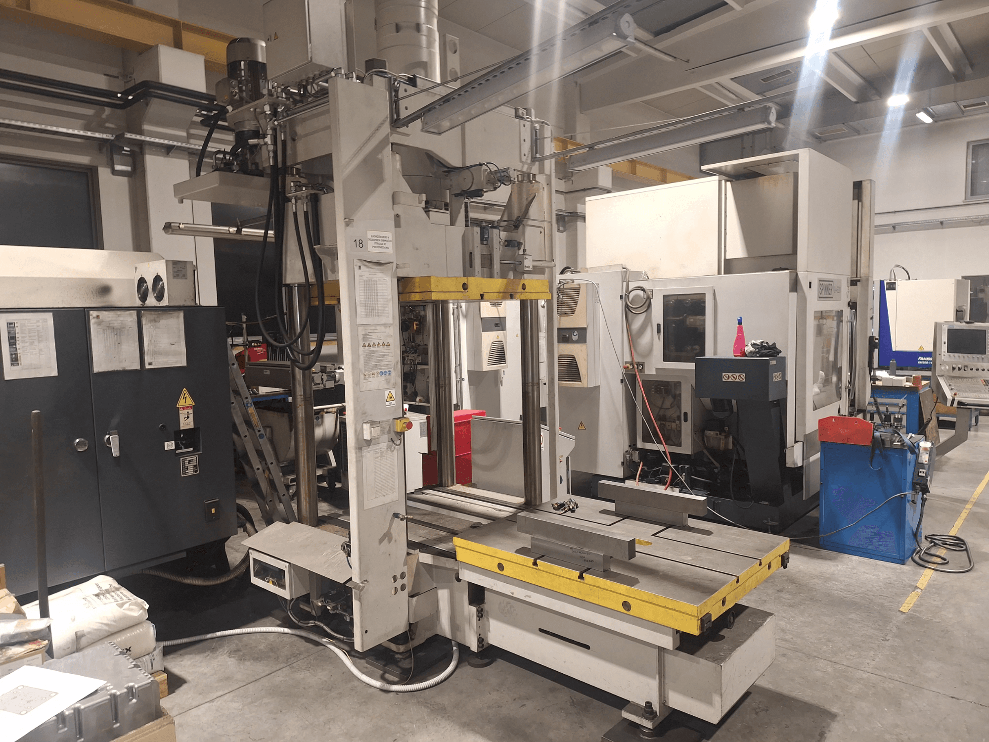 Frezarka pozioma Synergic, widok z przodu; wyposażona w szeroki stół i różne panele sterowania, w warunkach warsztatowych.