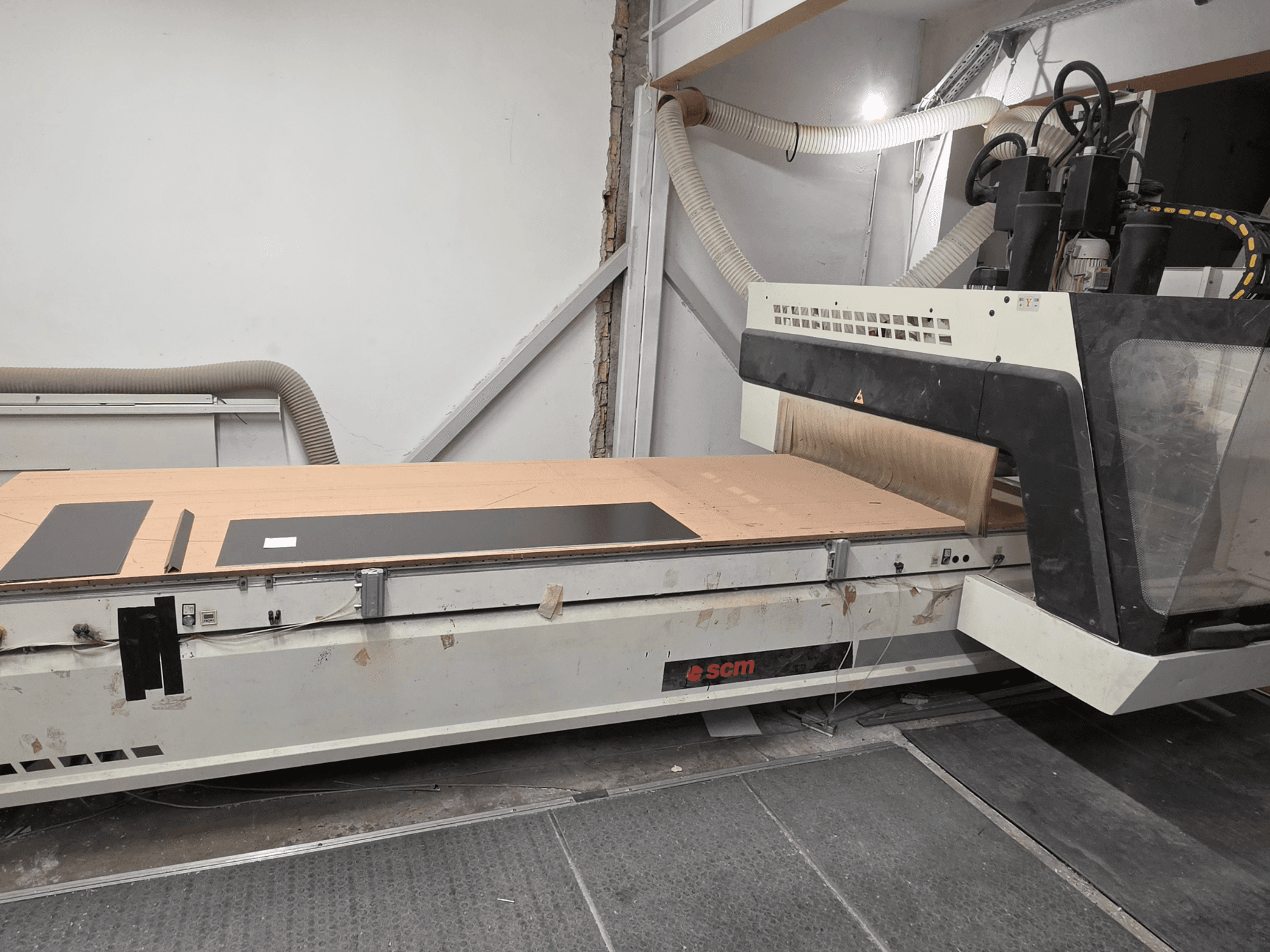 Centrum obróbki drewna CNC SCM RECORD 132 w widoku z boku, wyposażone w płaski stół roboczy z czarnymi elementami obrabianymi oraz system odpylania.