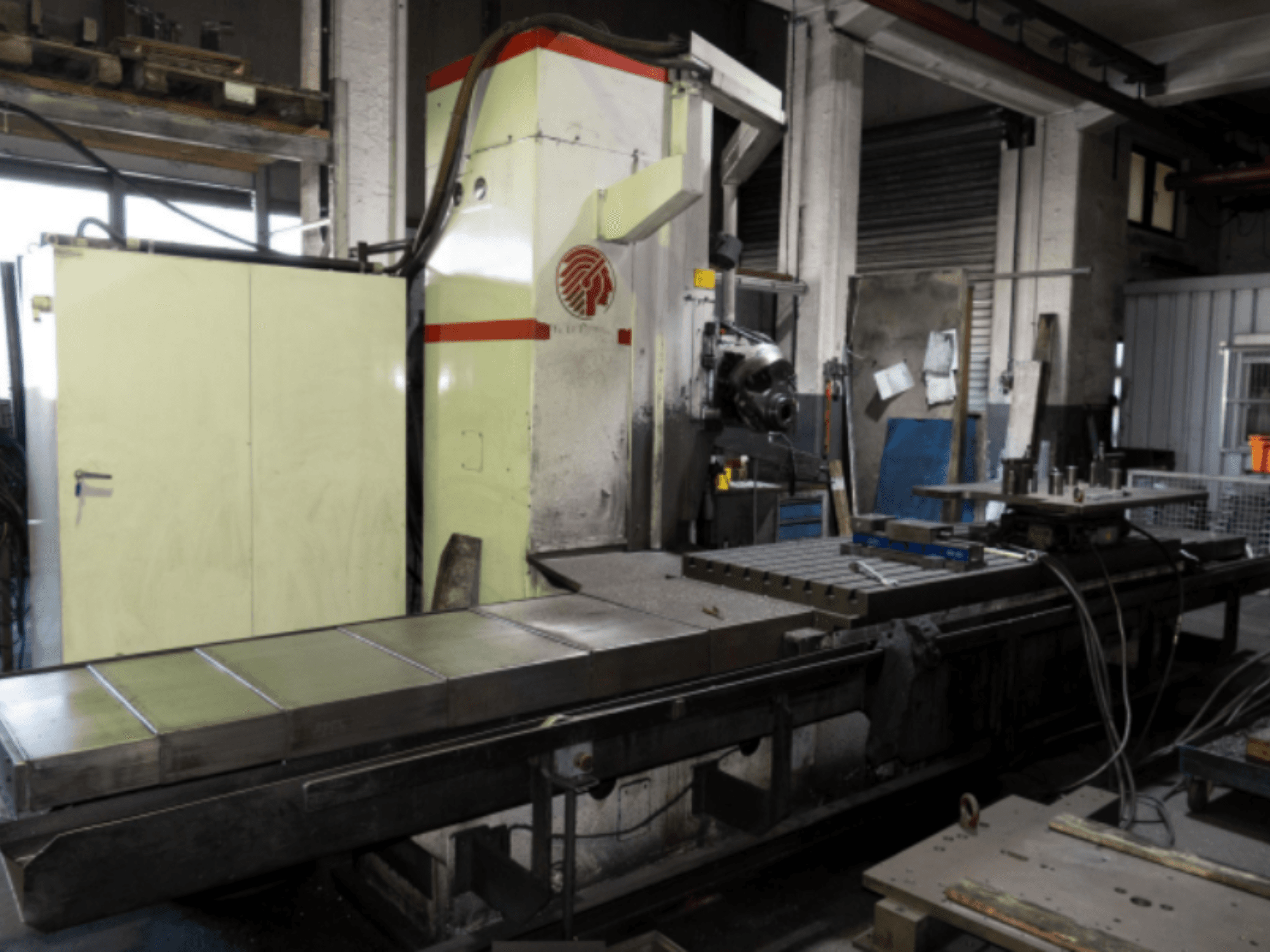 Frezarka przemysłowa z dużym stołem, widok z boku, prezentująca elementy sterujące i osprzęt w warunkach warsztatowych.