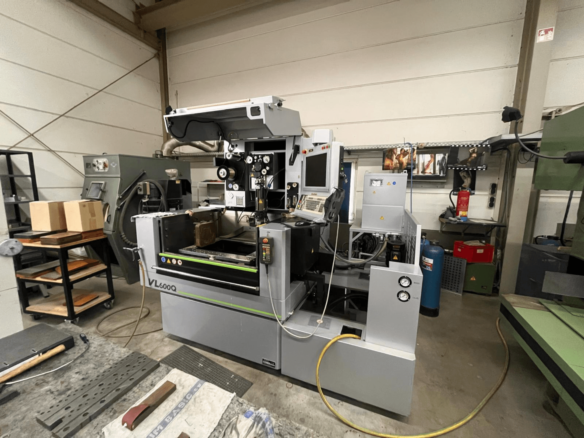 Maszyna CNC VL600Q w warsztacie, widok z przodu, z panelem sterowania, materiałem na miejscu i różnymi narzędziami w pobliżu.