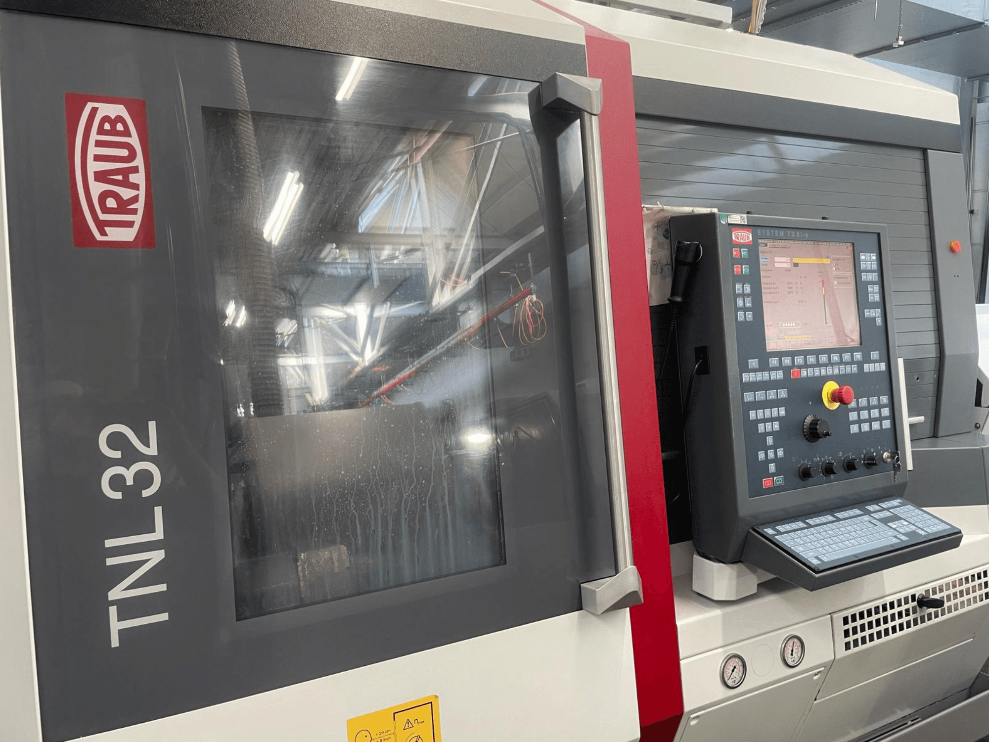 Widok z przodu tokarki CNC Traub TNL32 z panelem sterowania z przyciskami, wyświetlaczem i elegancką metalową obudową.