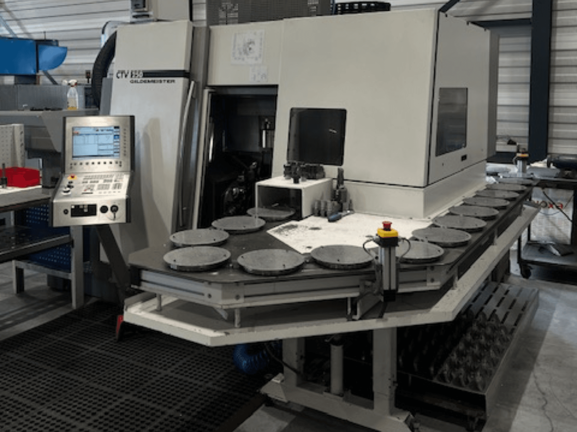 Alt text: Jednostka obróbcza CTV E33 Goldmeister w warsztacie, widok z przodu, z panelem sterowania i wieloma okrągłymi platformami roboczymi.