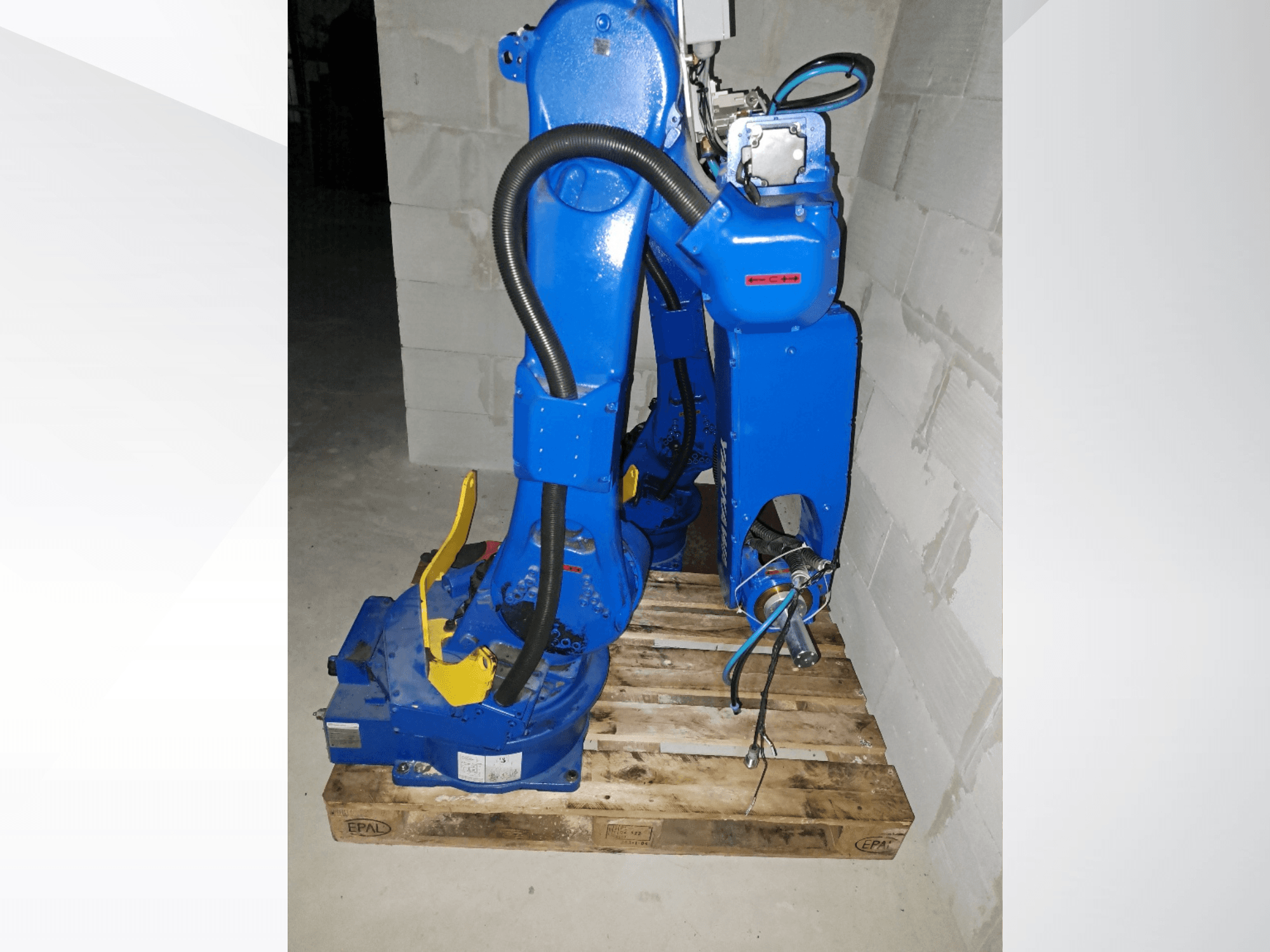 Ramię robota Yaskawa Motoman GP25 w kolorze niebieskim, widok z boku na drewnianej palecie, z widocznymi kablami i przegubami mechanicznymi.