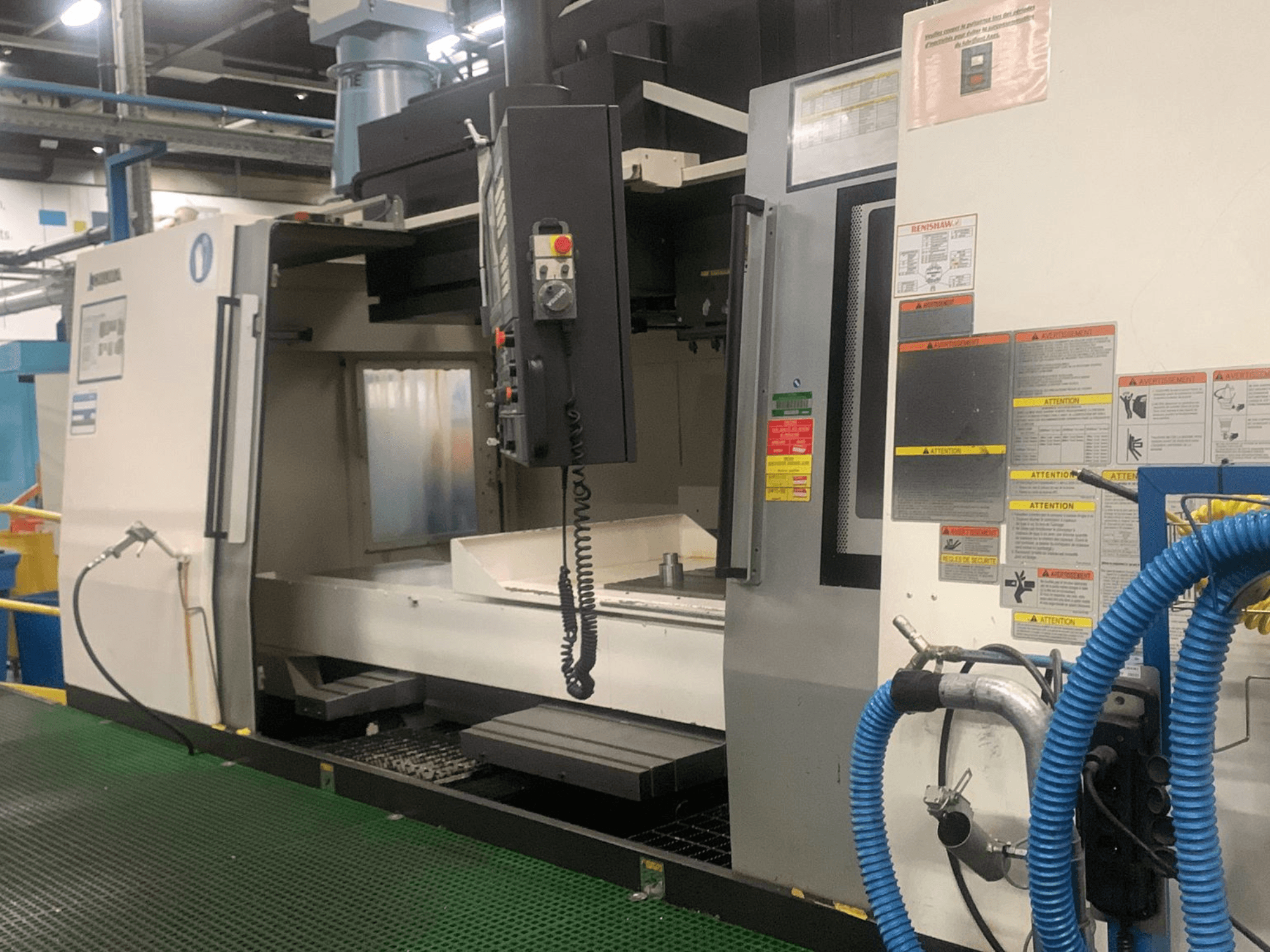 Pionowe centrum obróbcze Okuma Millac 852 VII, widok z przodu, przedstawiający panel sterowania, obszar wrzeciona oraz etykiety bezpieczeństwa.