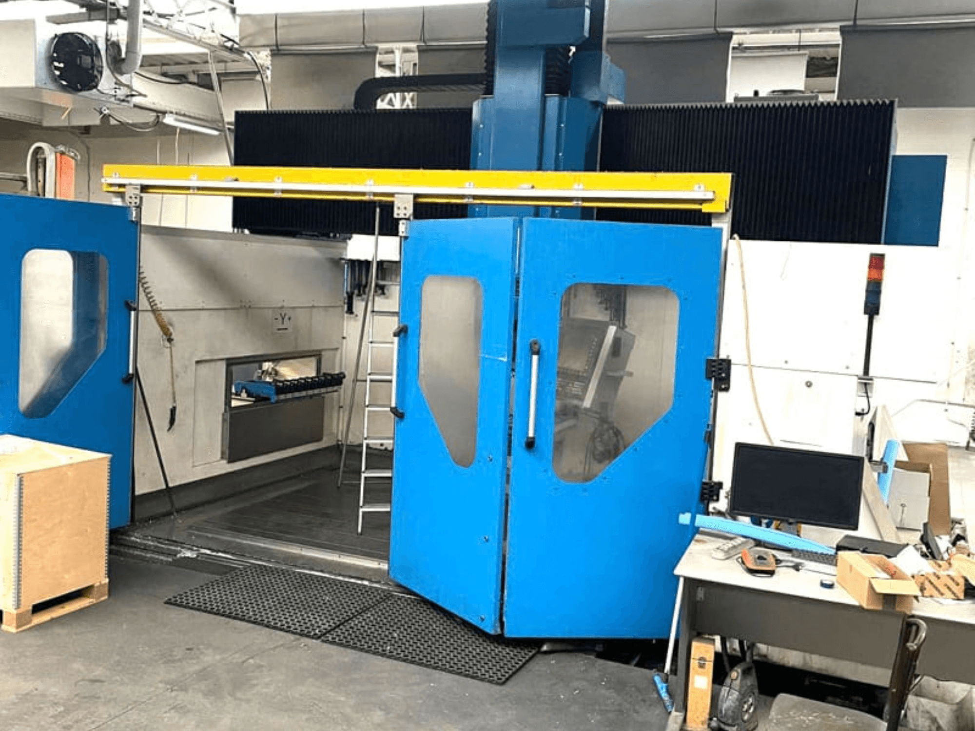 Widok z przodu pionowego centrum obróbczego TECHMILL LABOR SHAPE 3220 z otwartymi niebieskimi drzwiami, ukazujący obszar roboczy wewnątrz urządzenia.