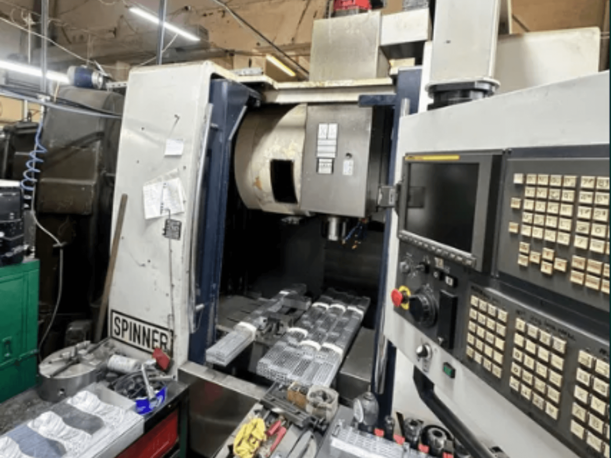 Maszyna CNC firmy Spinner, widok z przodu; posiada interfejs z ekranem dotykowym, narzędzia na obszarze roboczym i obrobione części gotowe do obróbki.
