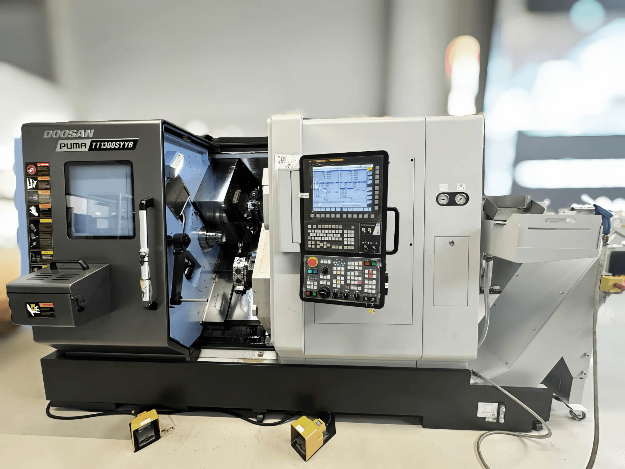 Centrum frezarskie Doosan Puma TT1300SYYB w widoku z boku, przedstawiające panel sterowania i wnętrze maszyny z widocznymi narzędziami.