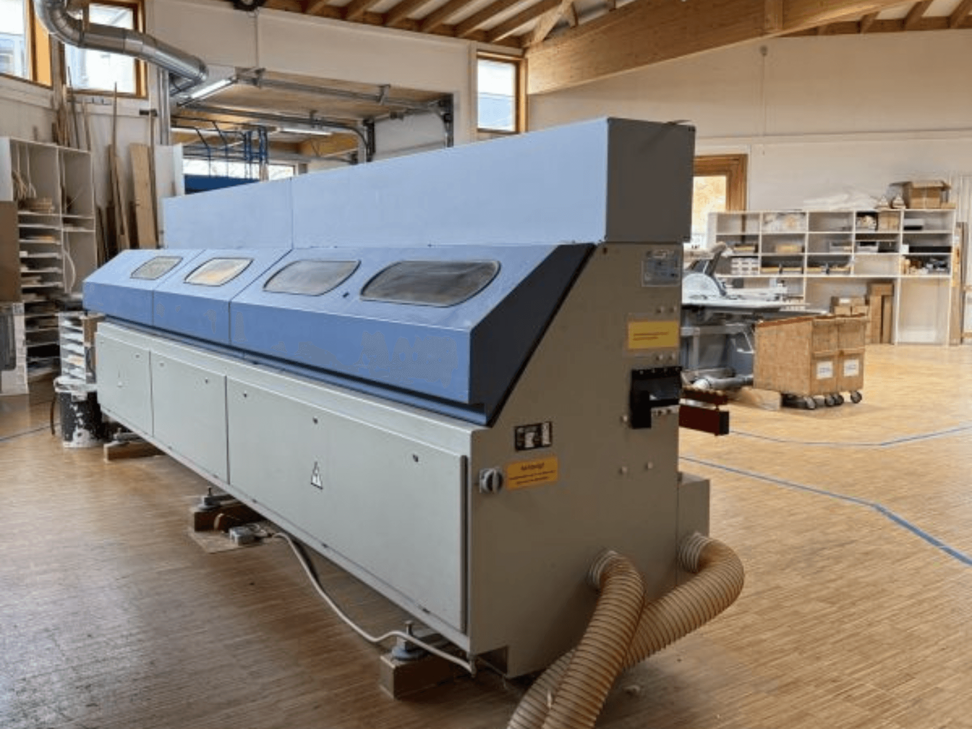 Okleiniarka OTT Pacific V6-F pokazana z boku; posiada długi niebieski blat i panel sterowania z mocowaniem węża.