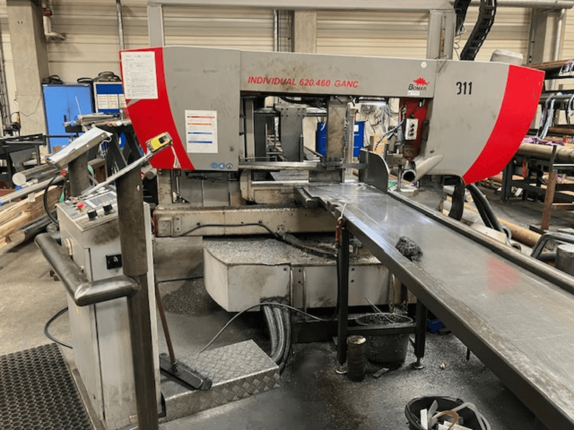 Piła taśmowa BOMAR INDIVIDUAL 620-460 GANC, widok z przodu, z elementami sterującymi, obszarem cięcia i tłem warsztatu przemysłowego.