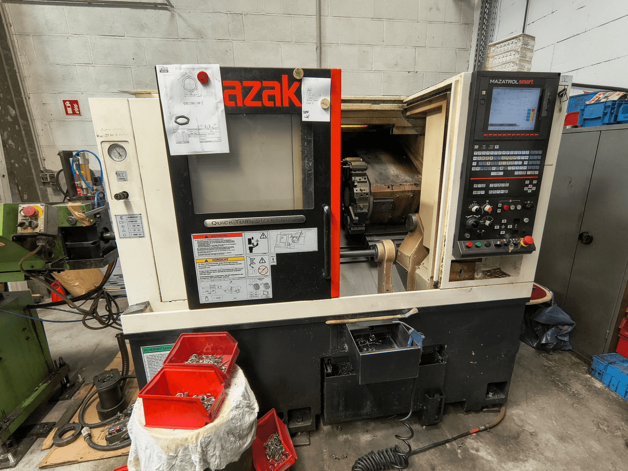 Mazak Quick Turn Smart 100 S – widok z boku przedstawiający panel sterowania, tacę na płyn chłodzący oraz pojemniki do przechowywania śrub.