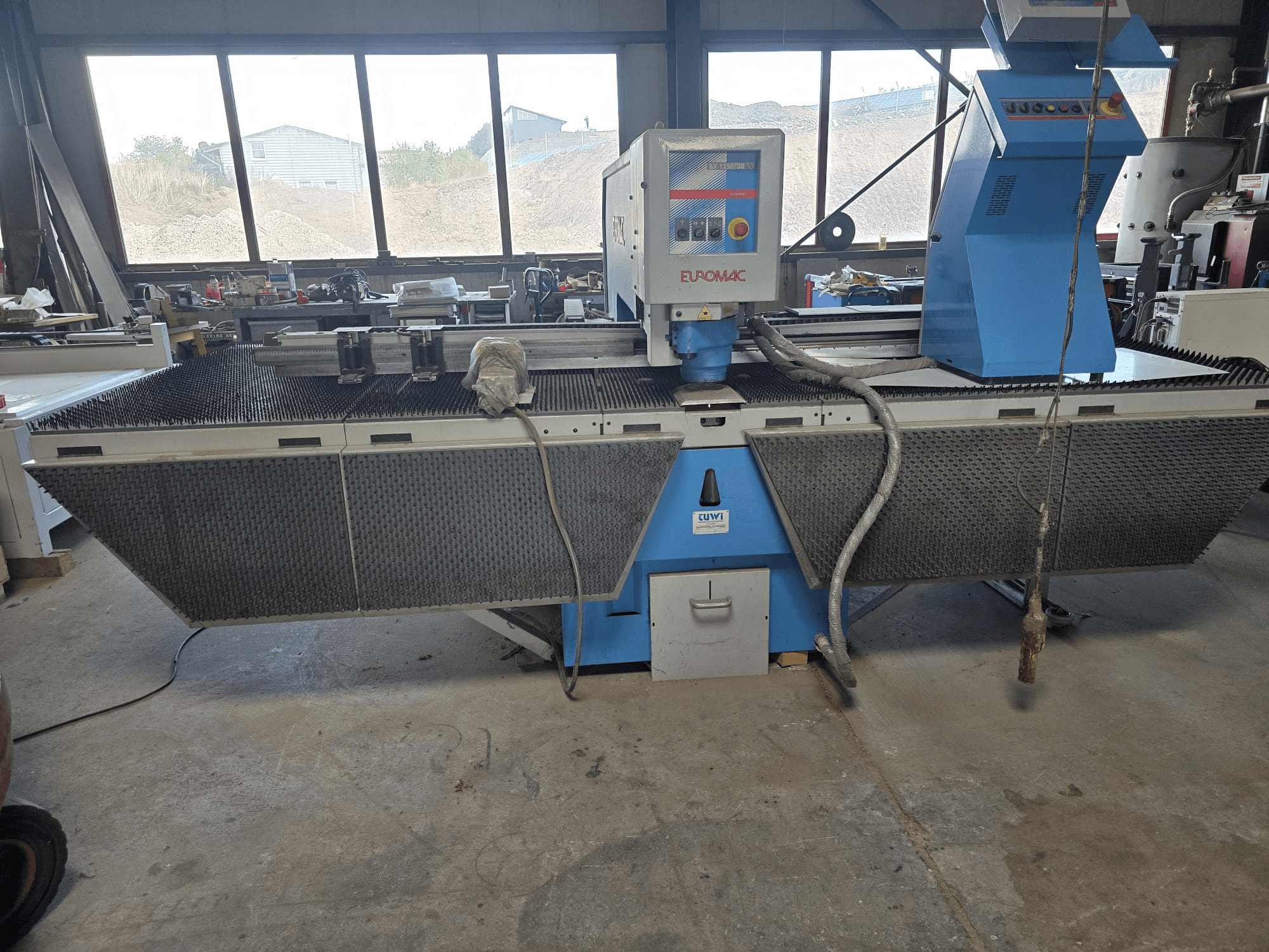 Wykrawarka CNC Euromac BX 1250/30 w warsztacie – widok z boku przedstawiający elementy sterujące, konstrukcję przemysłową oraz metalowy stół roboczy.