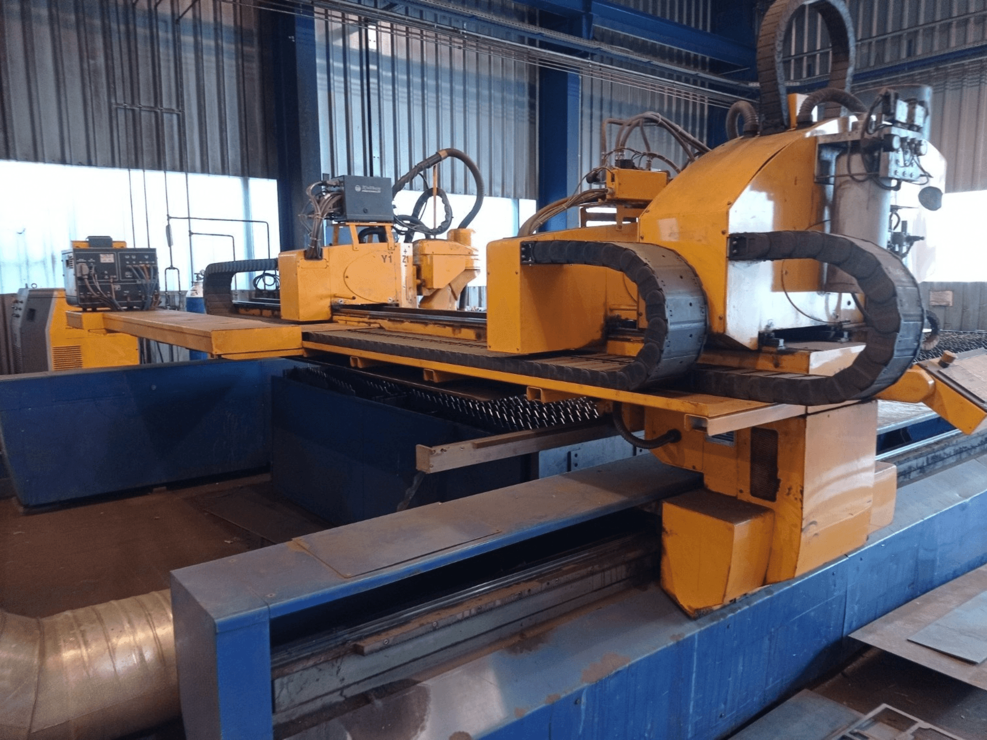 Żółta maszyna CNC do cięcia plazmowego z dwoma poziomymi ramionami, pokazana od przodu, z panelem sterowania i łożem do cięcia.