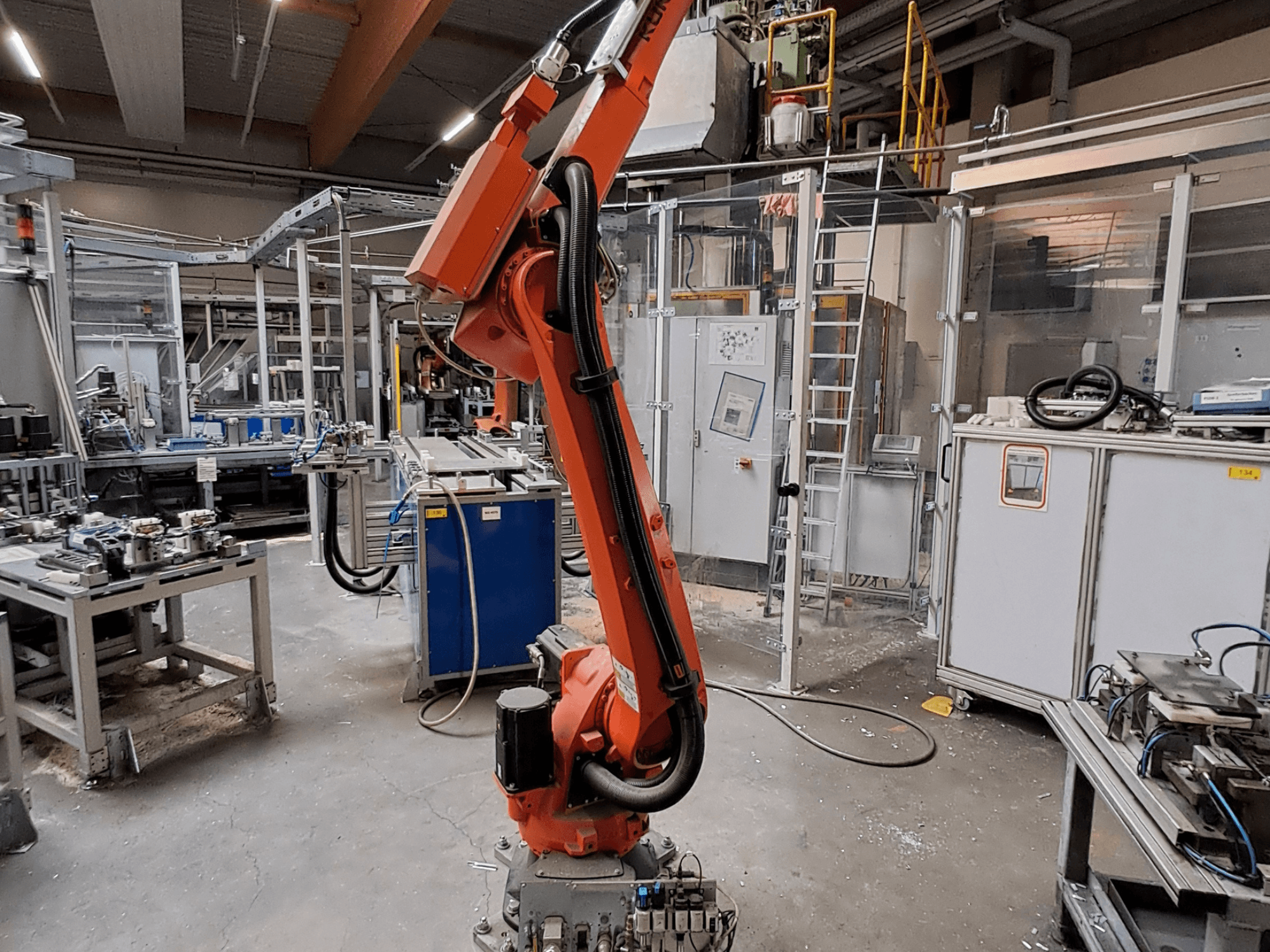Ramię robota KUKA KR 26 R3100/SEL w środowisku przemysłowym, widok z boku, z urządzeniami roboczymi w tle.