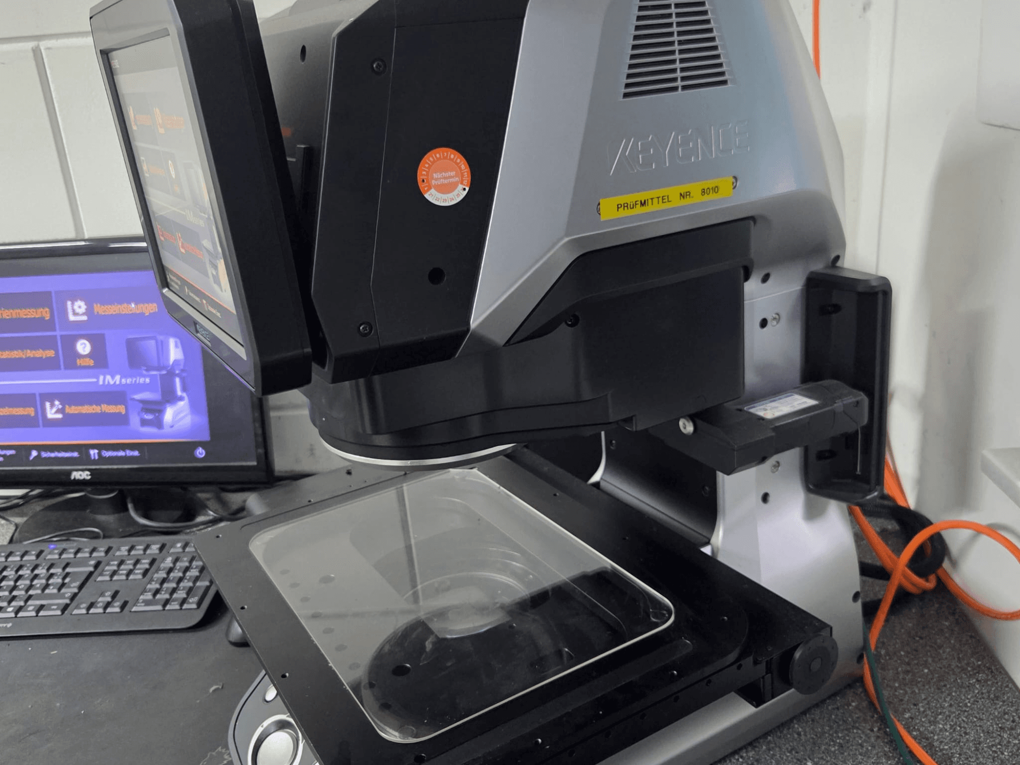 Optyczna maszyna pomiarowa KEYENCE IM 7030, widok z przodu z ekranem dotykowym i szklaną płytką pomiarową.