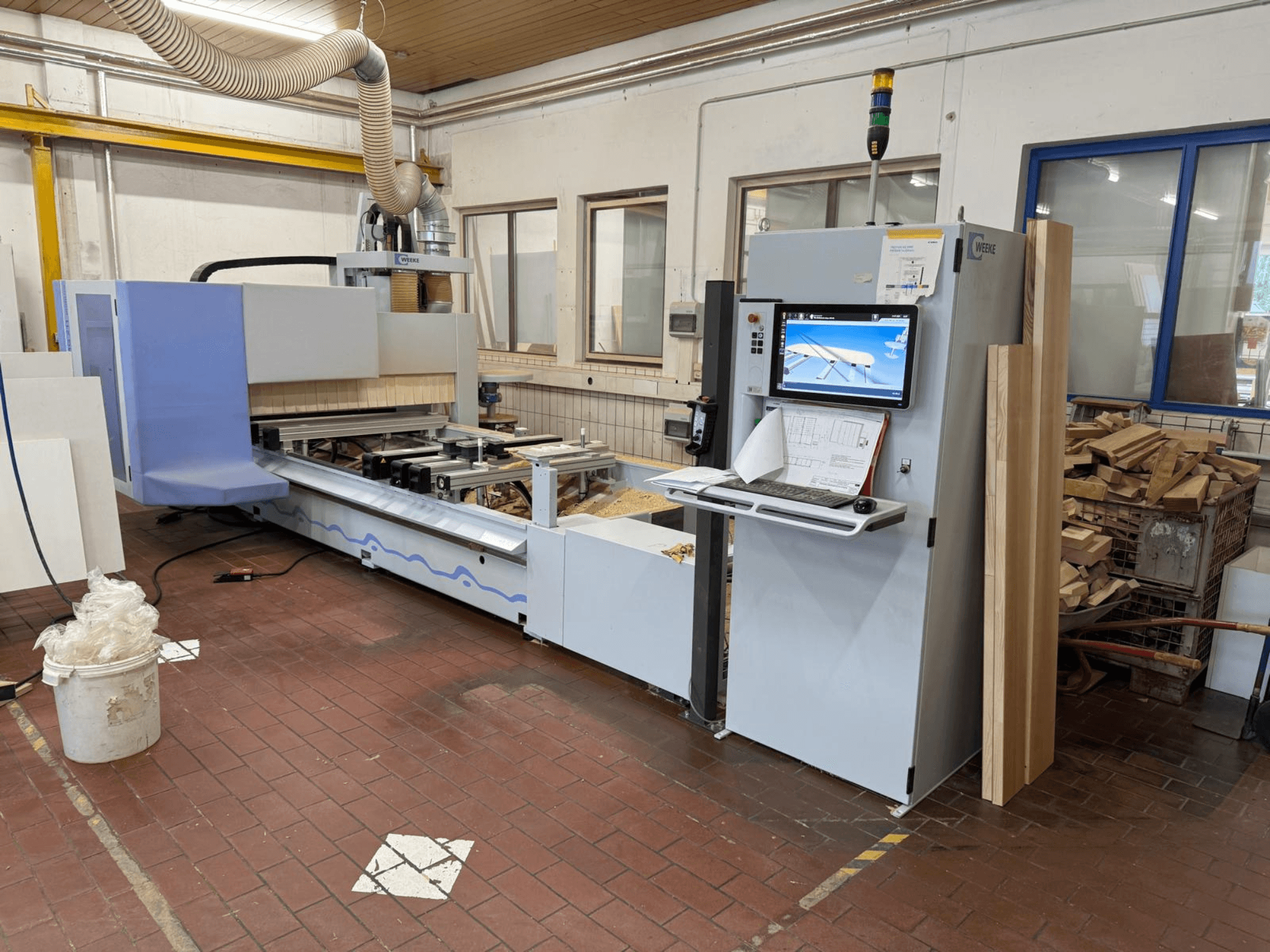 Centrum obróbki drewna CNC Weeke PROFI BMG211/32/12/K, widok z przodu, z panelem sterowania i elementami drewnianymi, wyposażone w system odpylania.