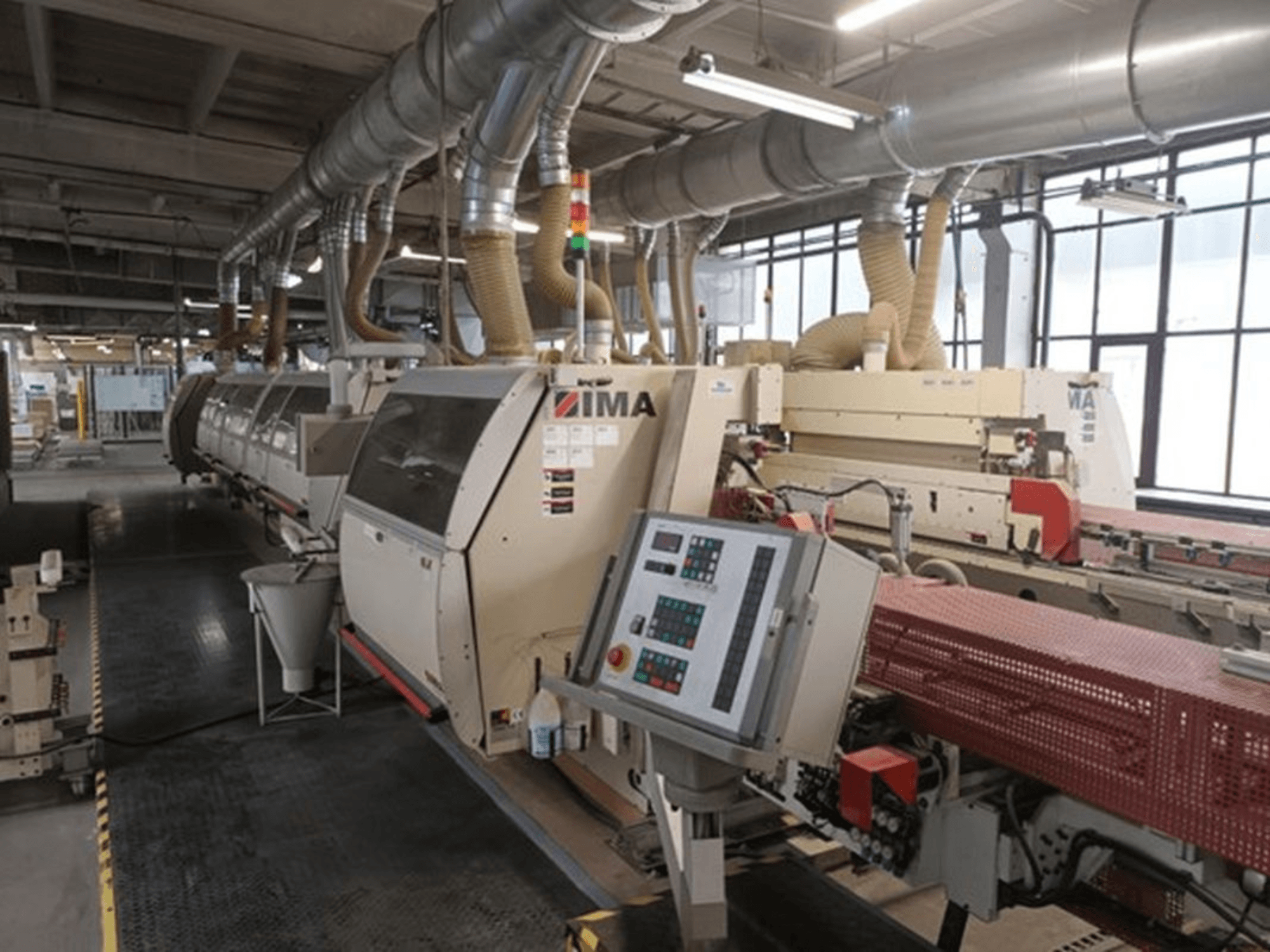 Maszyny przemysłowe IMA w fabryce, widok z przodu, z panelami sterowania i rurami odpylającymi.