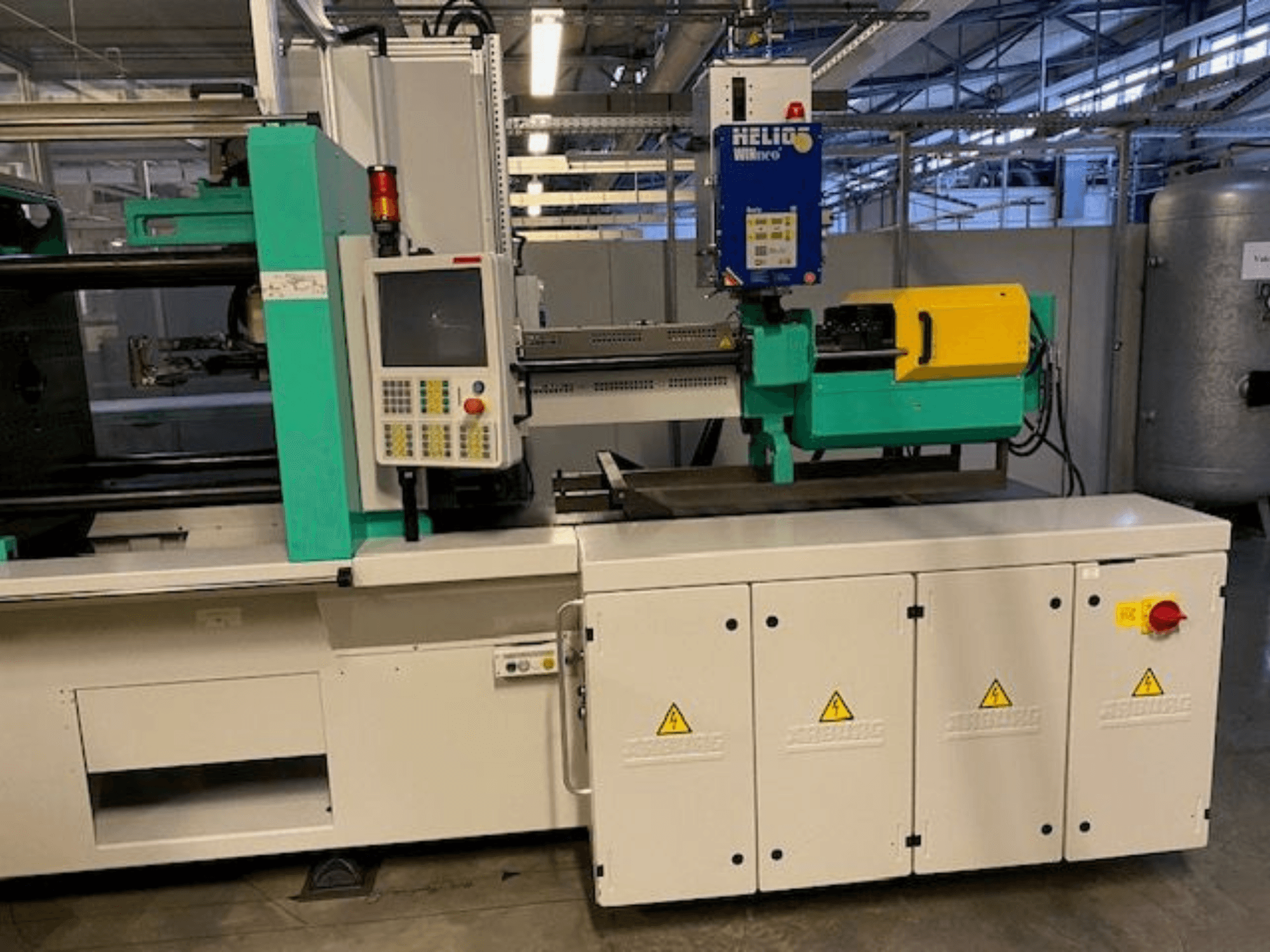 Wtryskarka przemysłowa, model HELIO, widok z przodu, z panelem sterowania, osłonami bezpieczeństwa i przyciskiem zatrzymania awaryjnego.