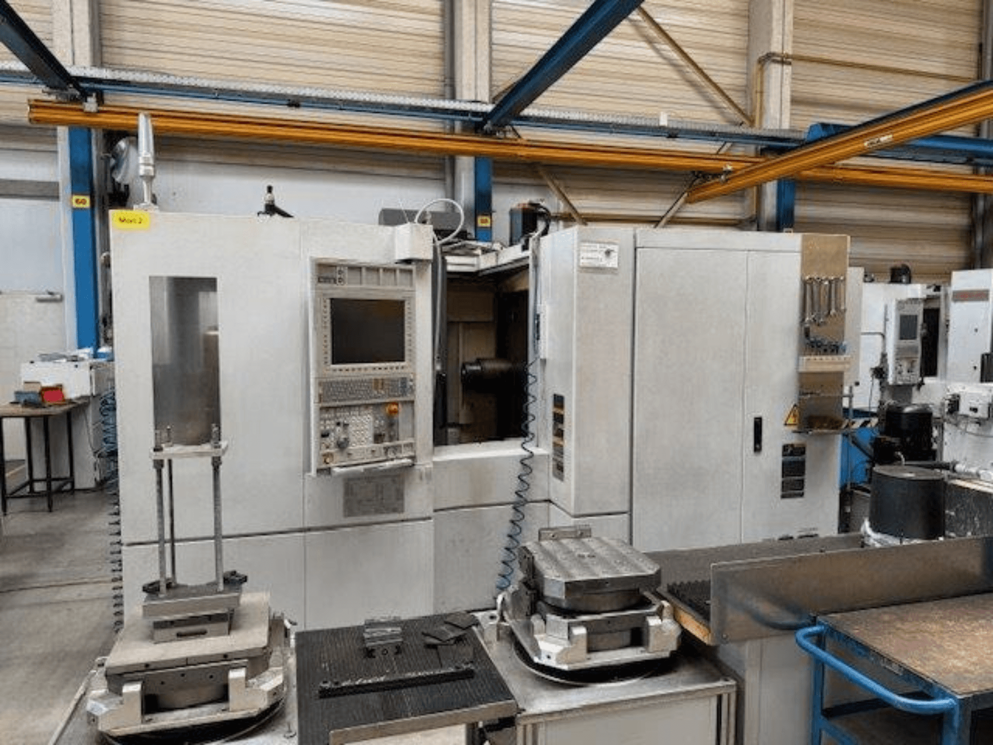 MORI SEIKI NH4000 DCG widok z przodu poziomego centrum obróbczego z panelem sterowania i elementami obrabianymi na stole.