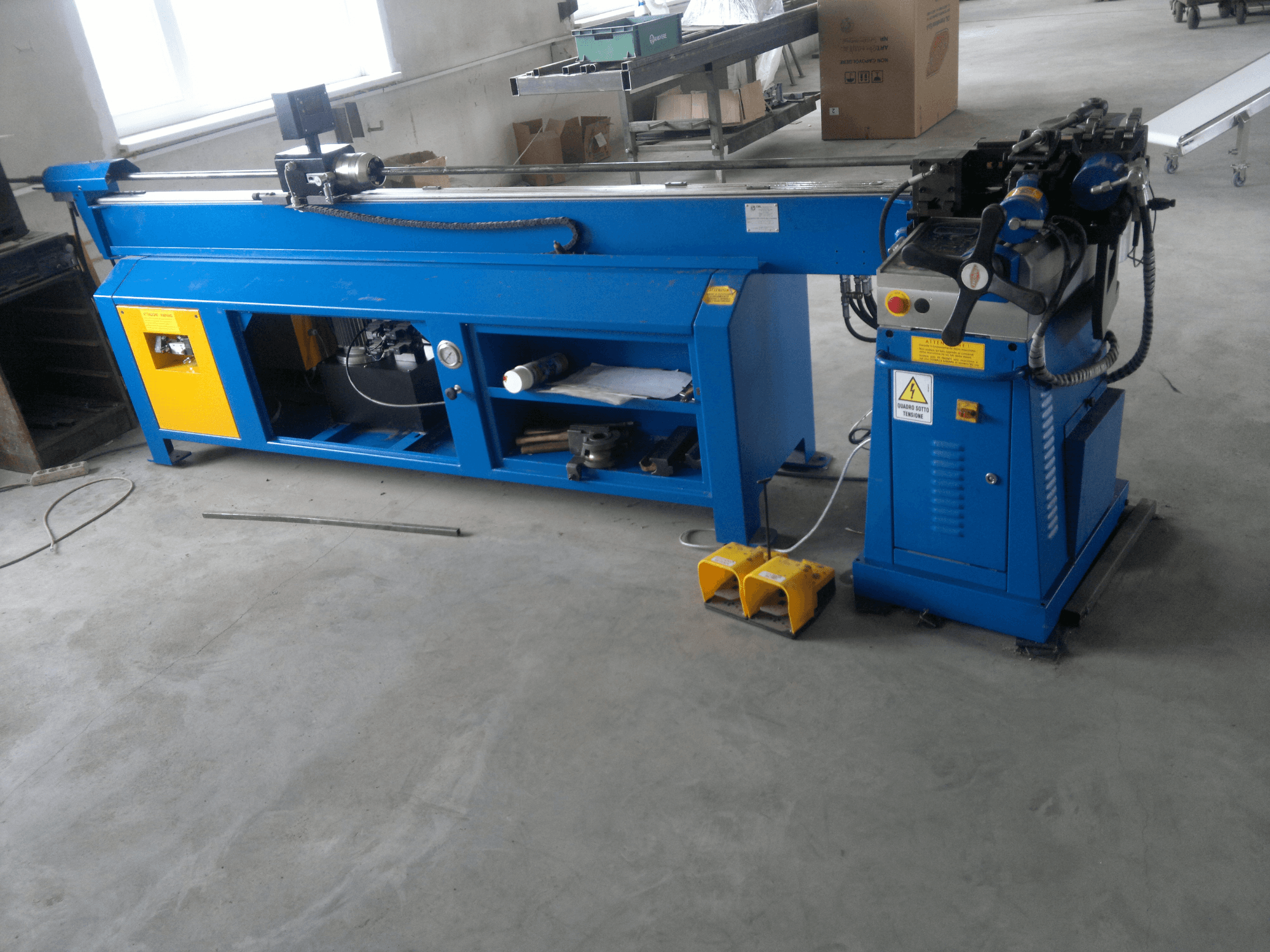 Niebieska maszyna do obróbki drewna z żółtymi akcentami, widok z boku; posiada panel sterowania, pedały nożne i zespół obrotowego ostrza.