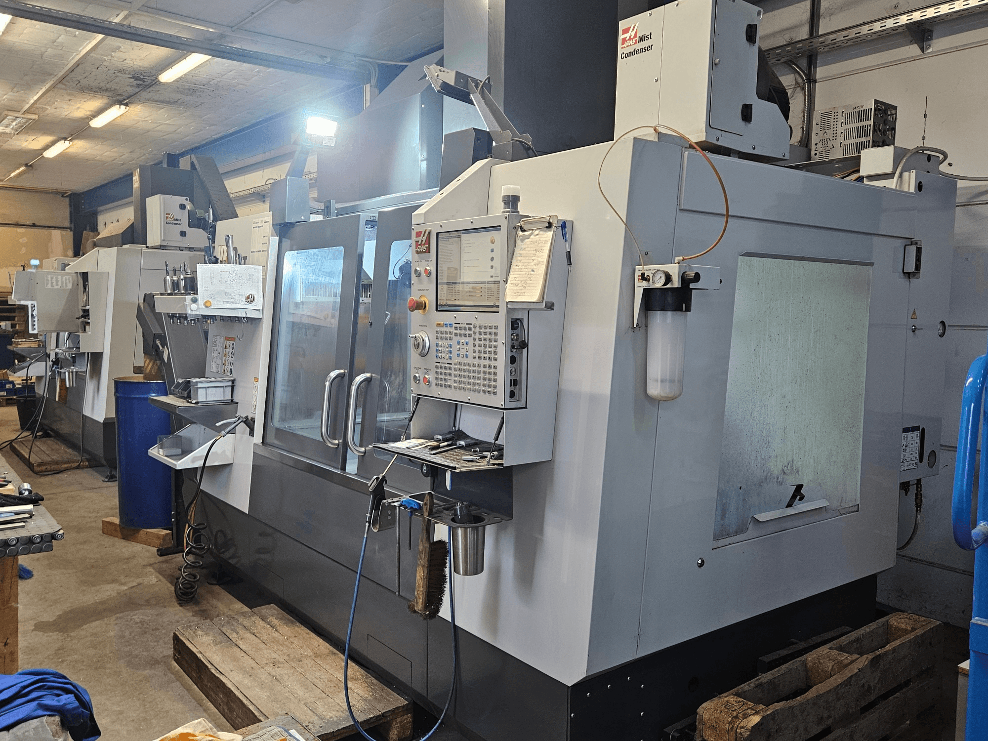 Pionowe centrum obróbcze Haas VF-3YT/50 w warsztacie – widok z przodu przedstawiający panel sterowania, uchwyty narzędziowe oraz skraplacz mgły.