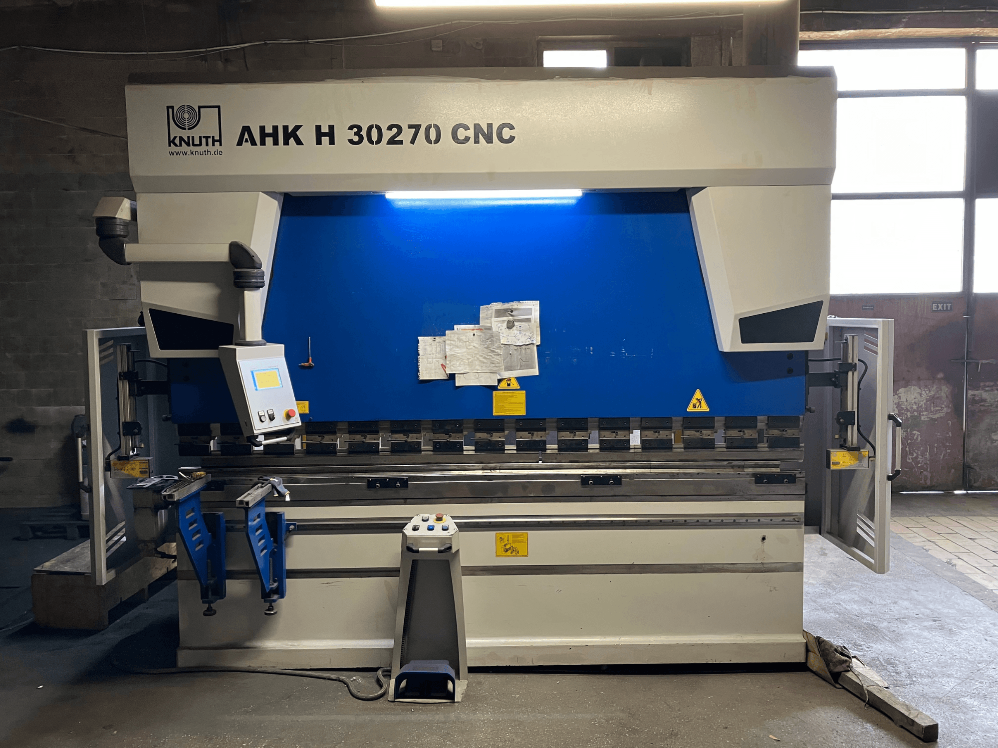 Prasa krawędziowa KNUTH AHK H 30270 z sterowaniem CNC w warsztacie, widok z przodu, z widocznym panelem sterowania i niebiesko-białą kolorystyką, z otwartymi drzwiami bocznymi.