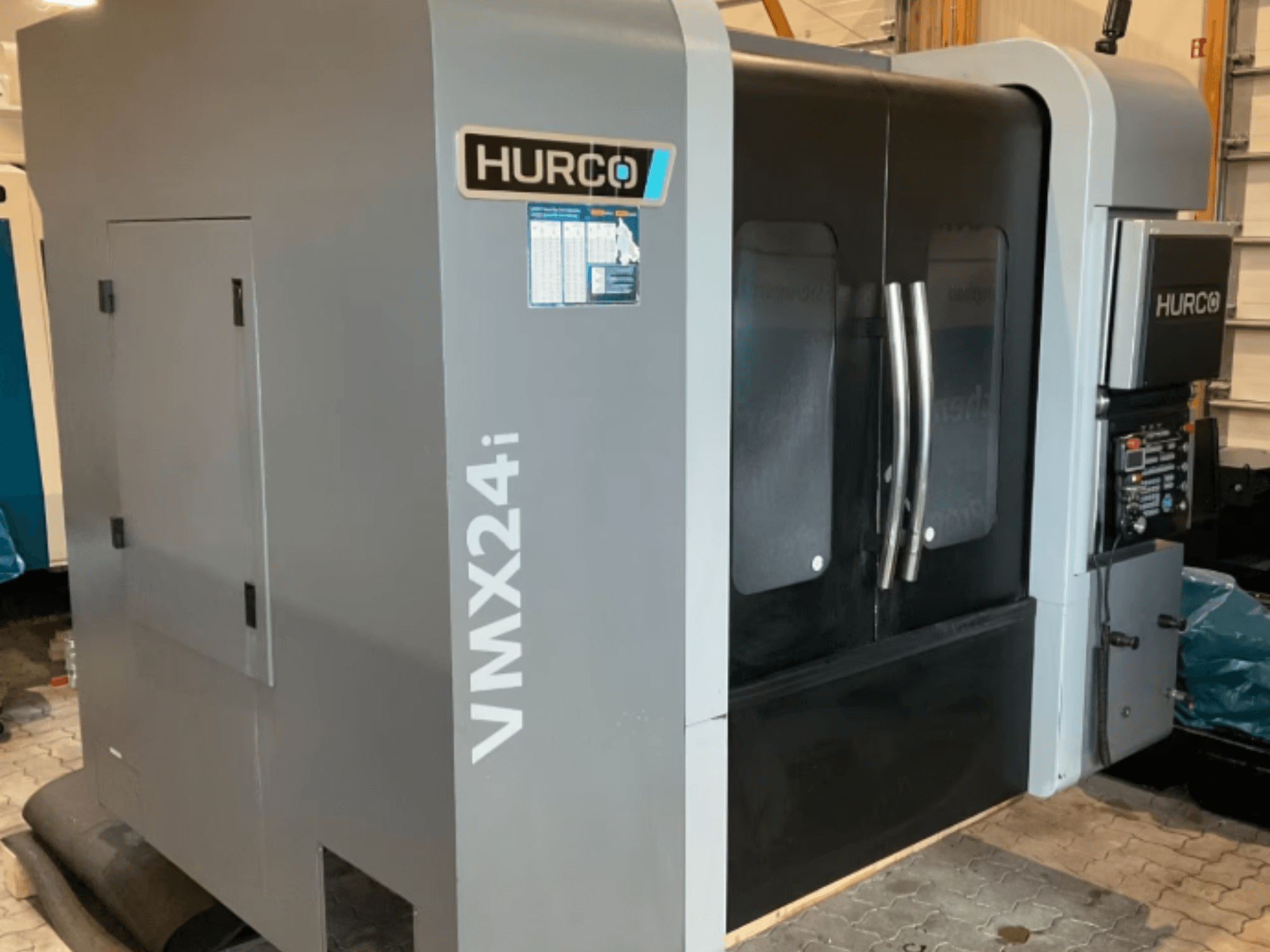 Pionowe centrum obróbcze Hurco VMX 24i, widok z przodu: obudowa w kolorze metalicznej szarości, czarne drzwiczki panelowe oraz panel sterowania.