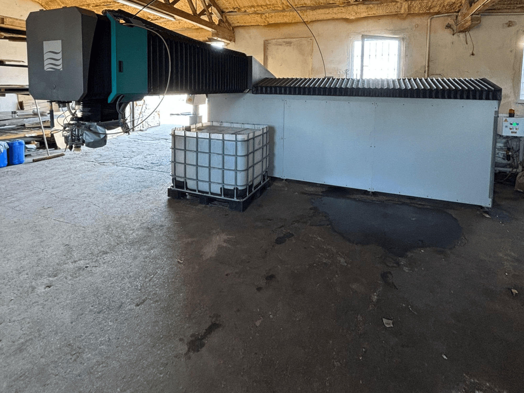 Przemysłowa maszyna strumieniowa w warsztacie, widok z boku, z dużym zbiornikiem wody i panelem sterowania widocznym obok.