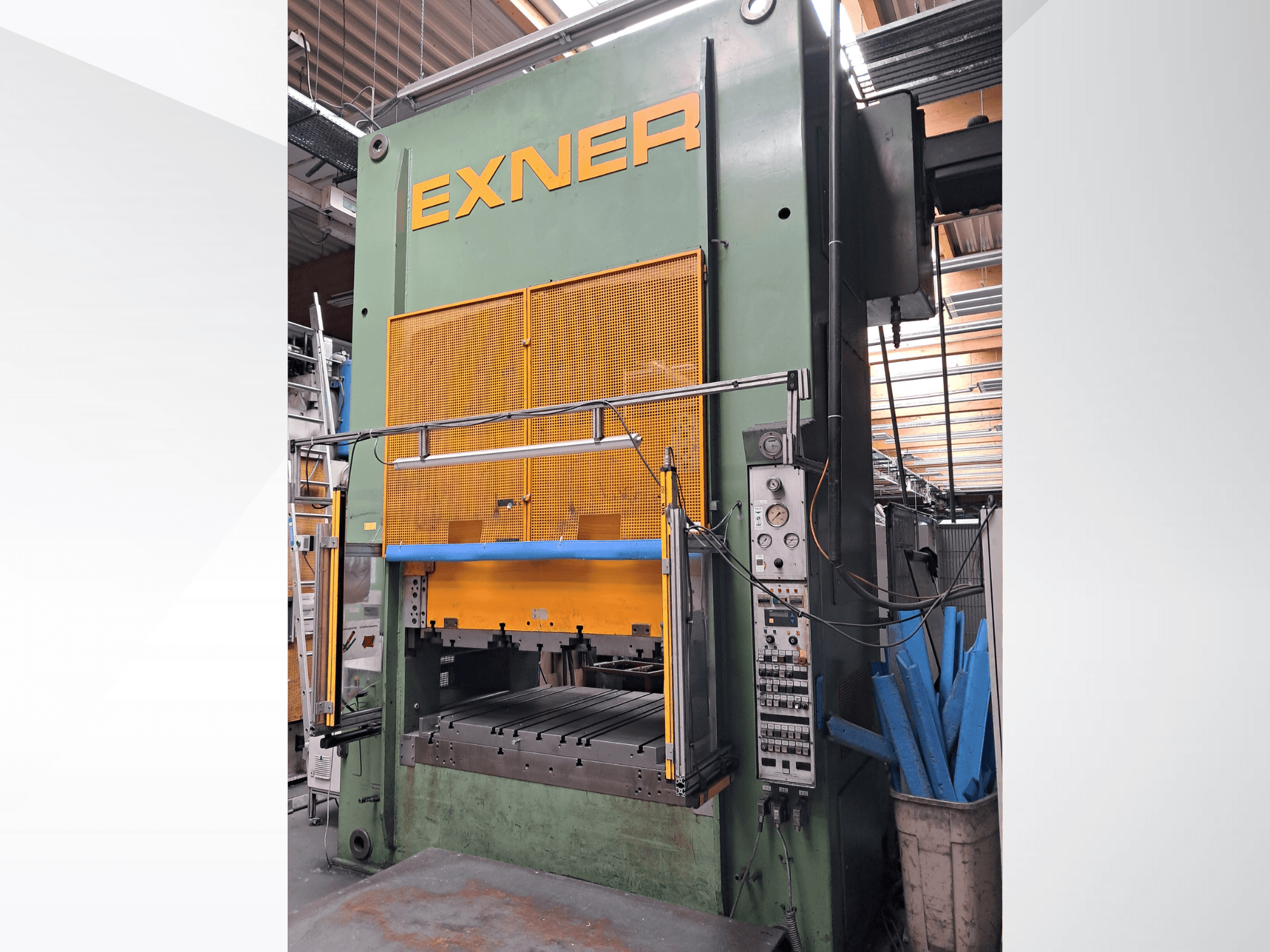 Prasa hydrauliczna EXNER EX SBR 150, widok z przodu; wyposażona w elementy sterujące, niebieską listwę zabezpieczającą i osłonę z siatki, umieszczona w środowisku warsztatowym.