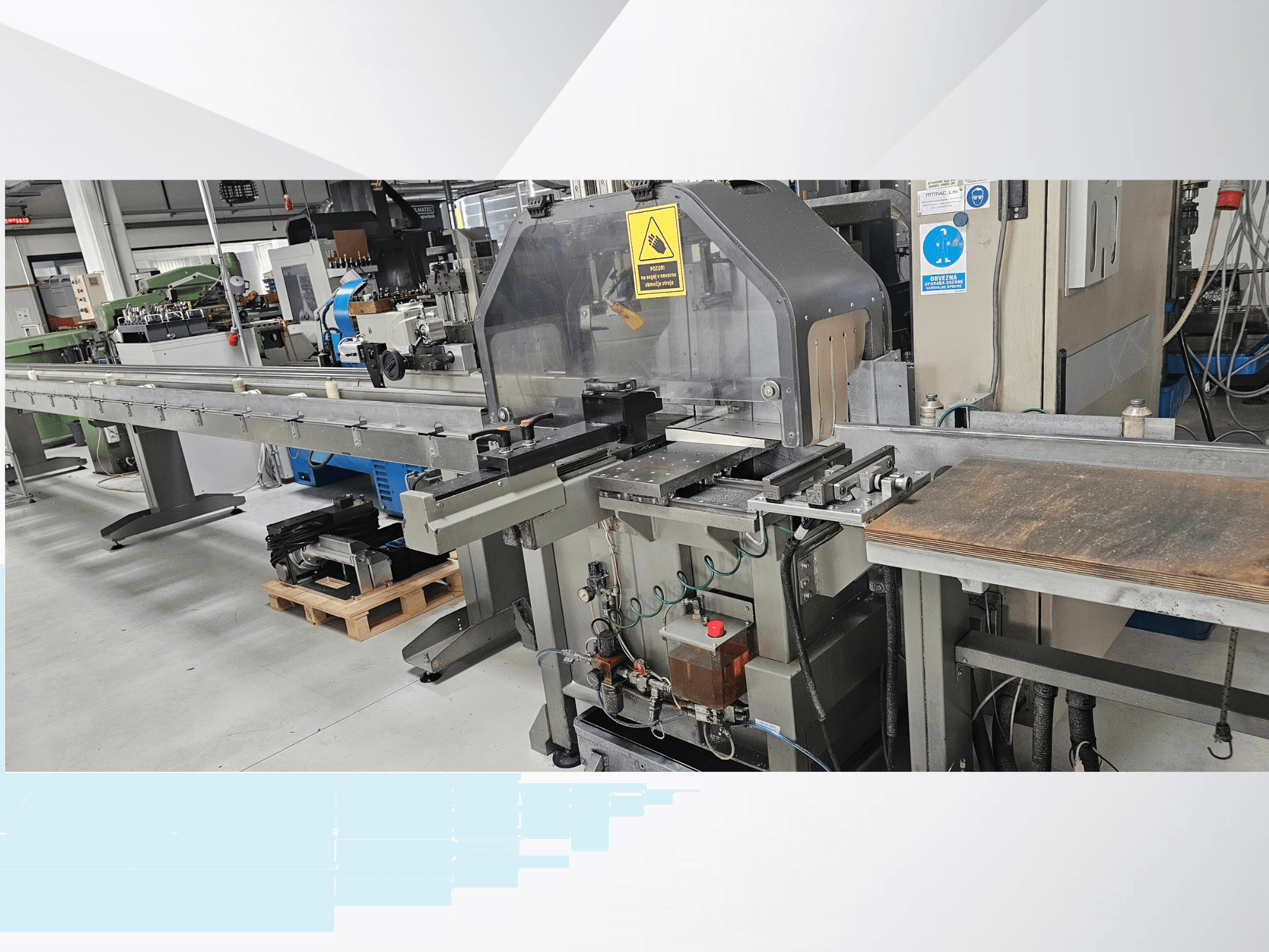 Przemysłowa przecinarka w widoku z boku, z długim przenośnikiem, panelem sterowania i ostrzeżeniami dotyczącymi bezpieczeństwa.